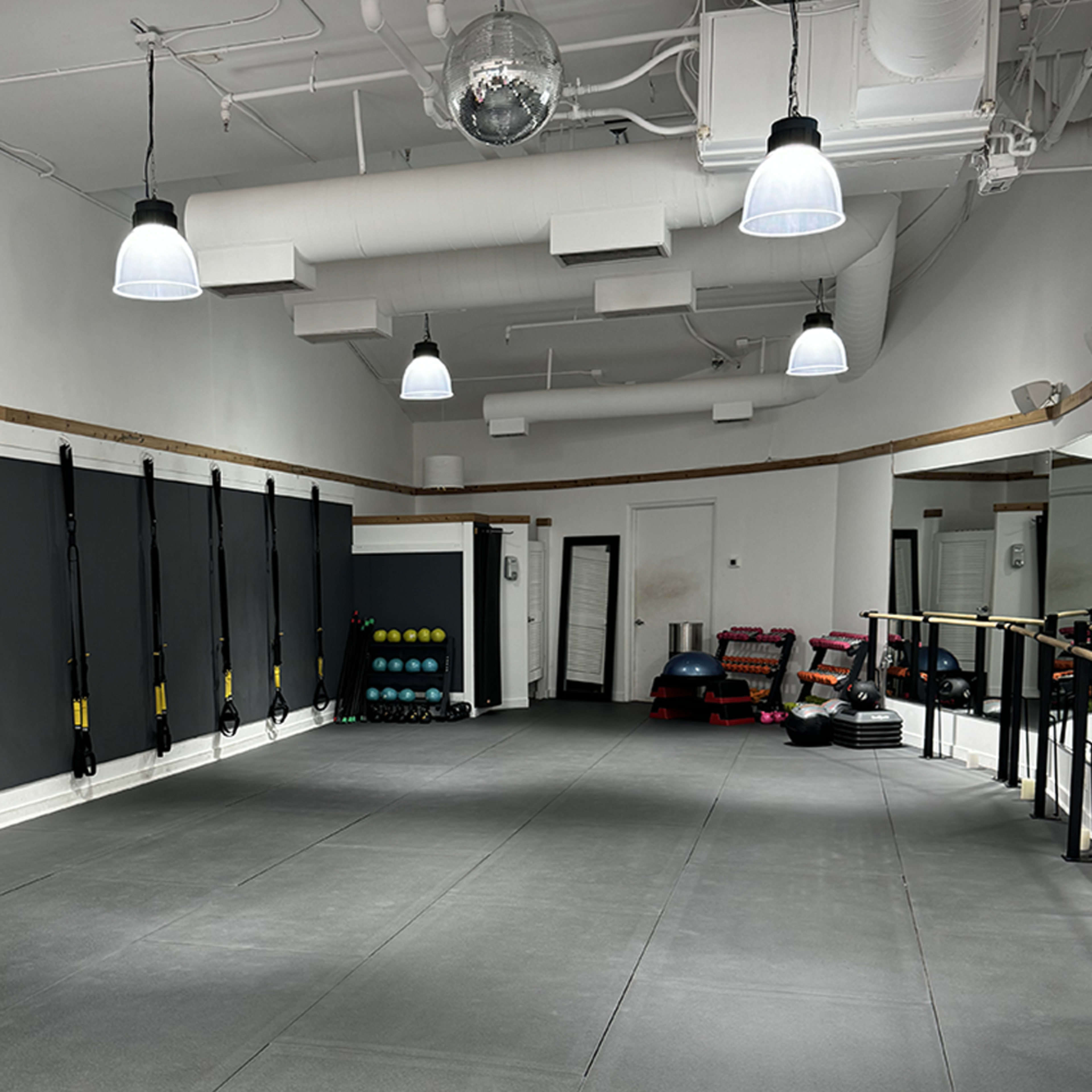 A spacious gym interior with gray flooring, wall-mounted fitness equipment, and various types of weights organized in a corner.