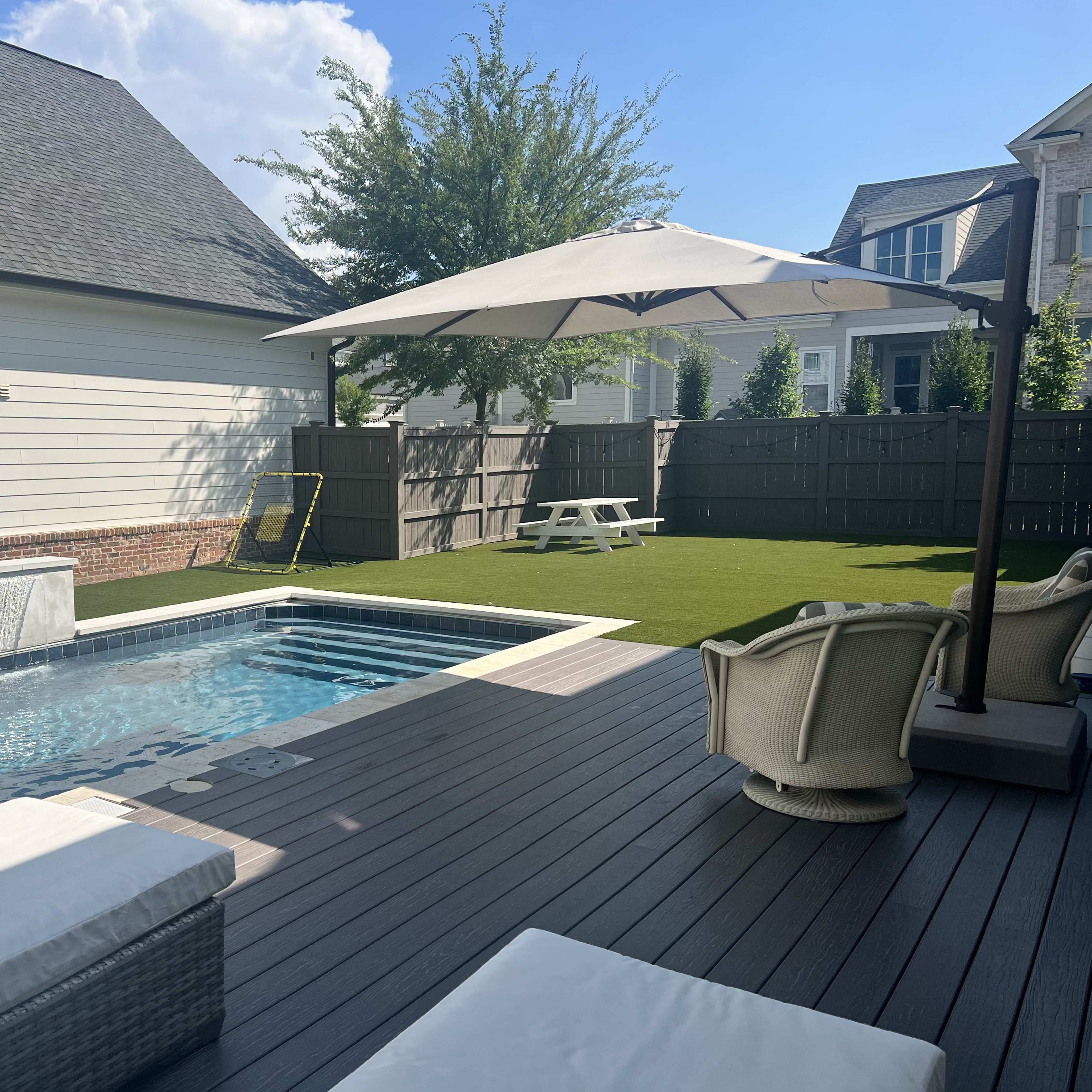 A backyard with a small swimming pool, a covered seating area, and artificial grass alongside a picnic table.