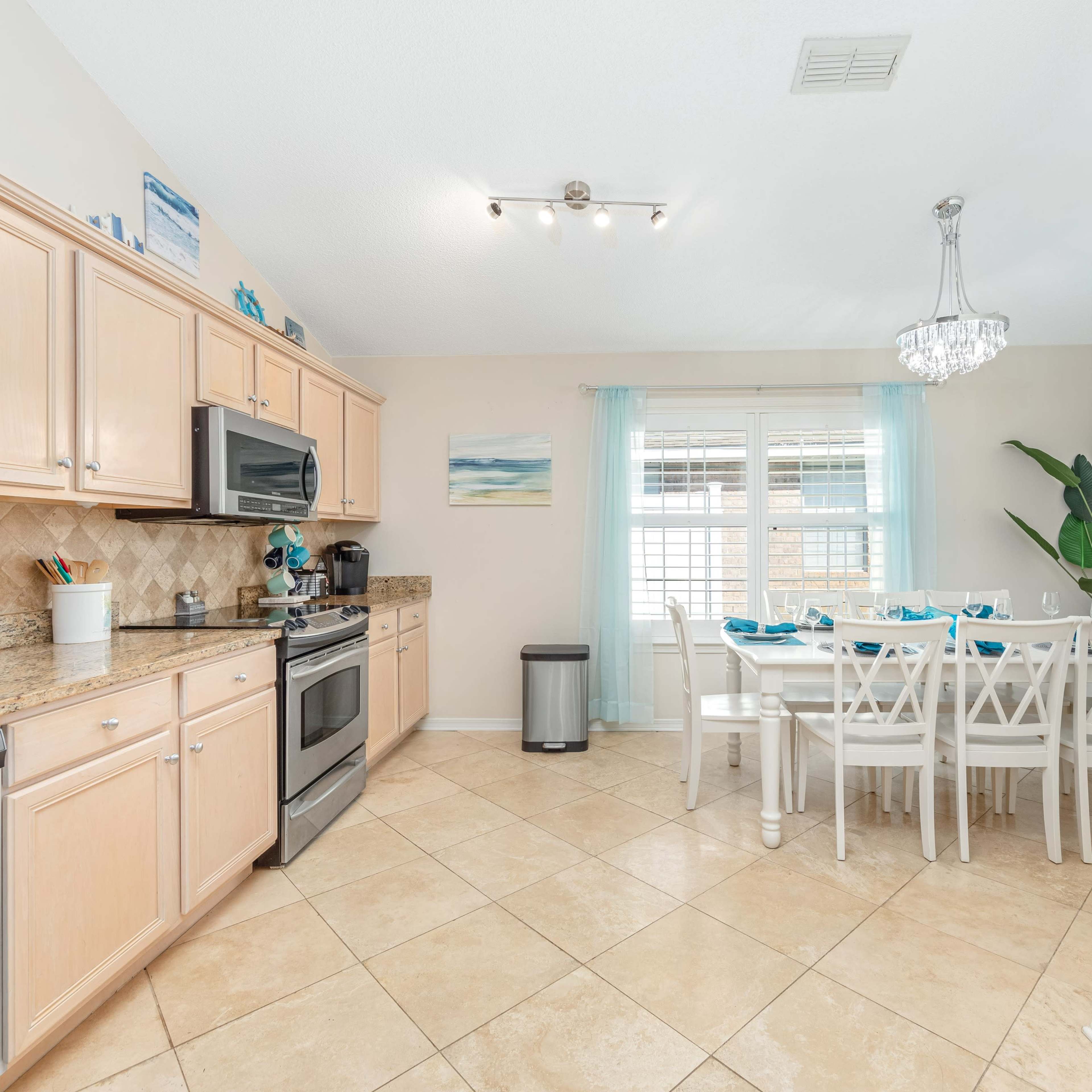 A modern kitchen features light wood cabinets, stainless steel appliances, and a dining area with a large table set for six.