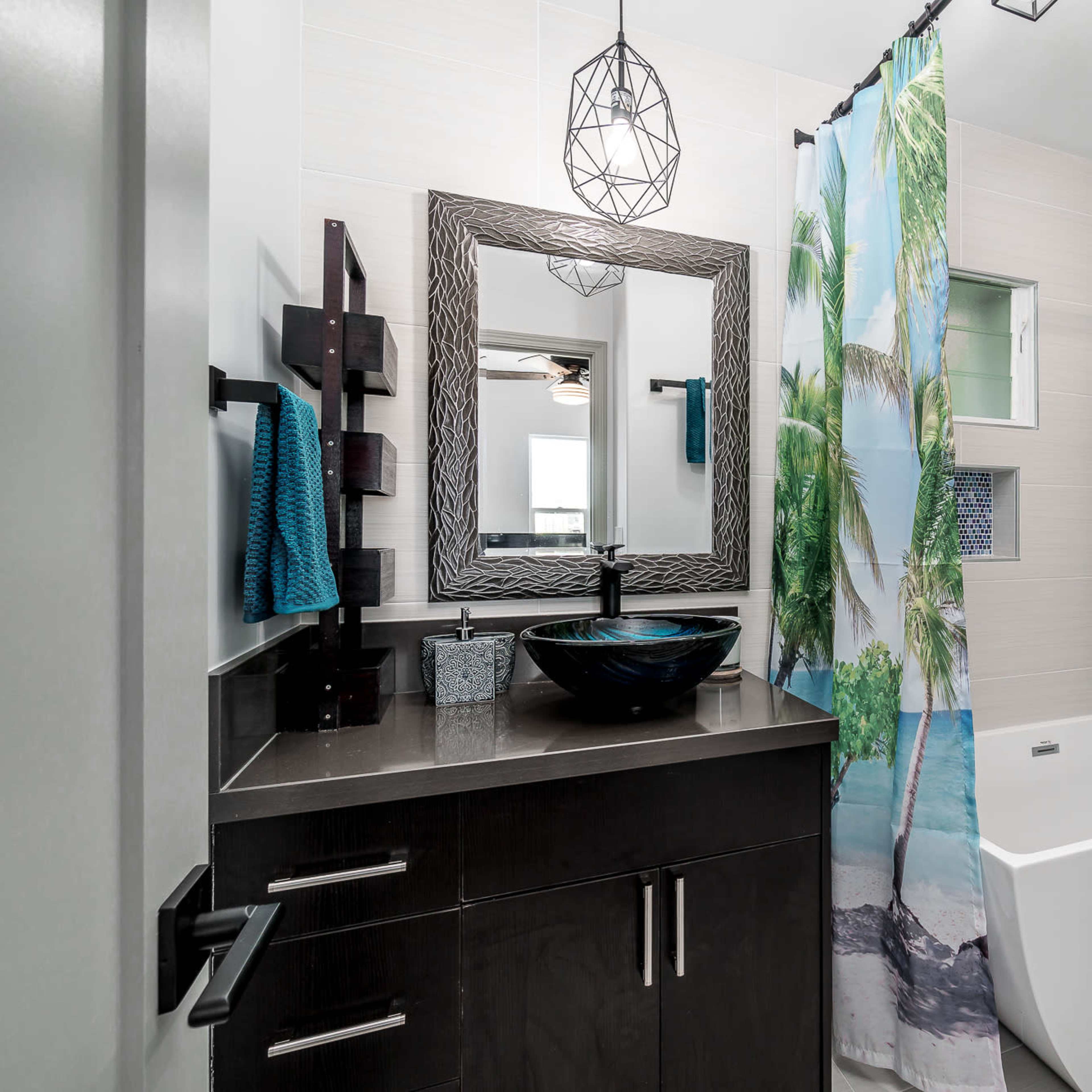 A modern bathroom featuring a freestanding bathtub, a large mirror, and a shower with curtains depicting palm trees.