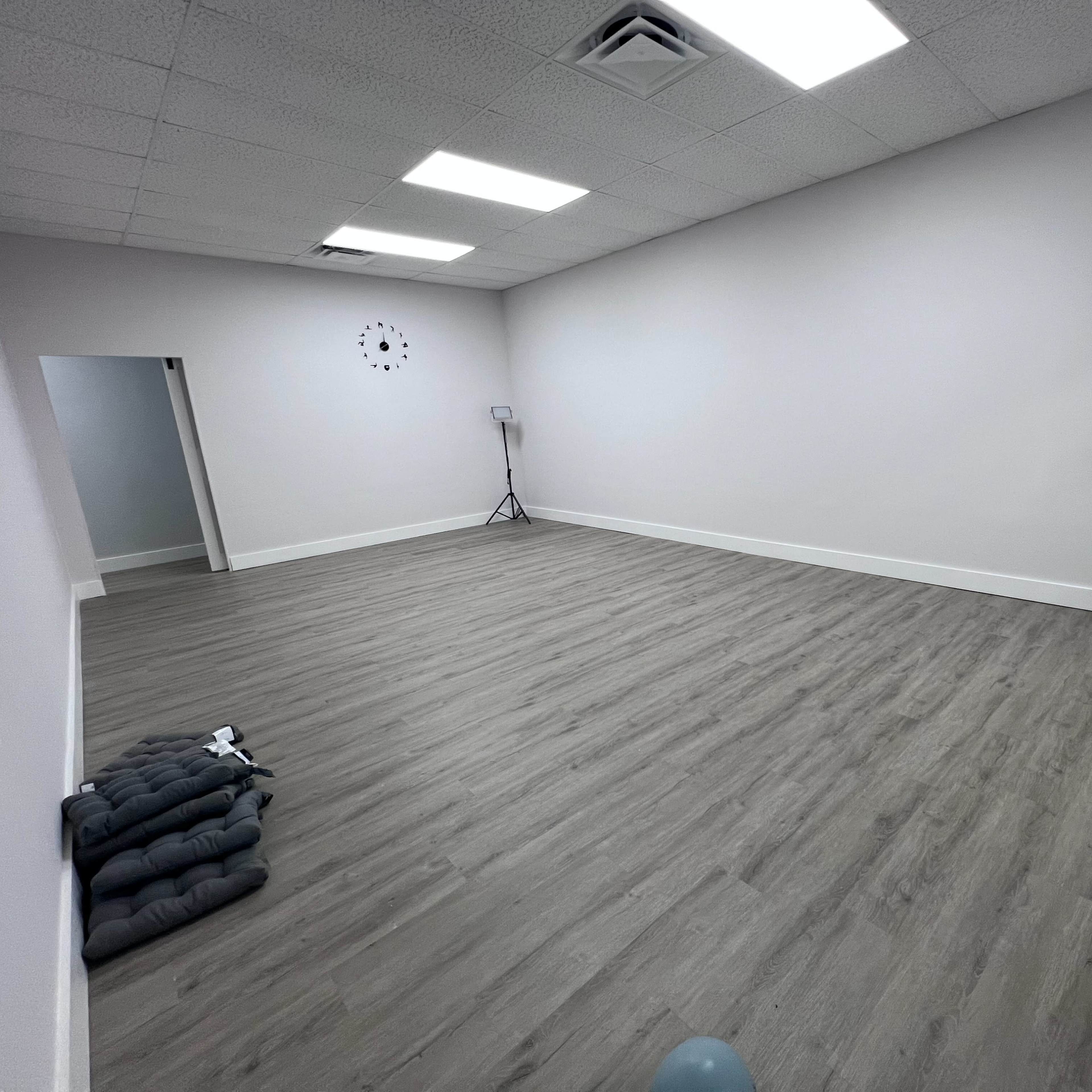 A spacious, empty room with light gray walls, a hardwood floor, and a large mirror on one side.
