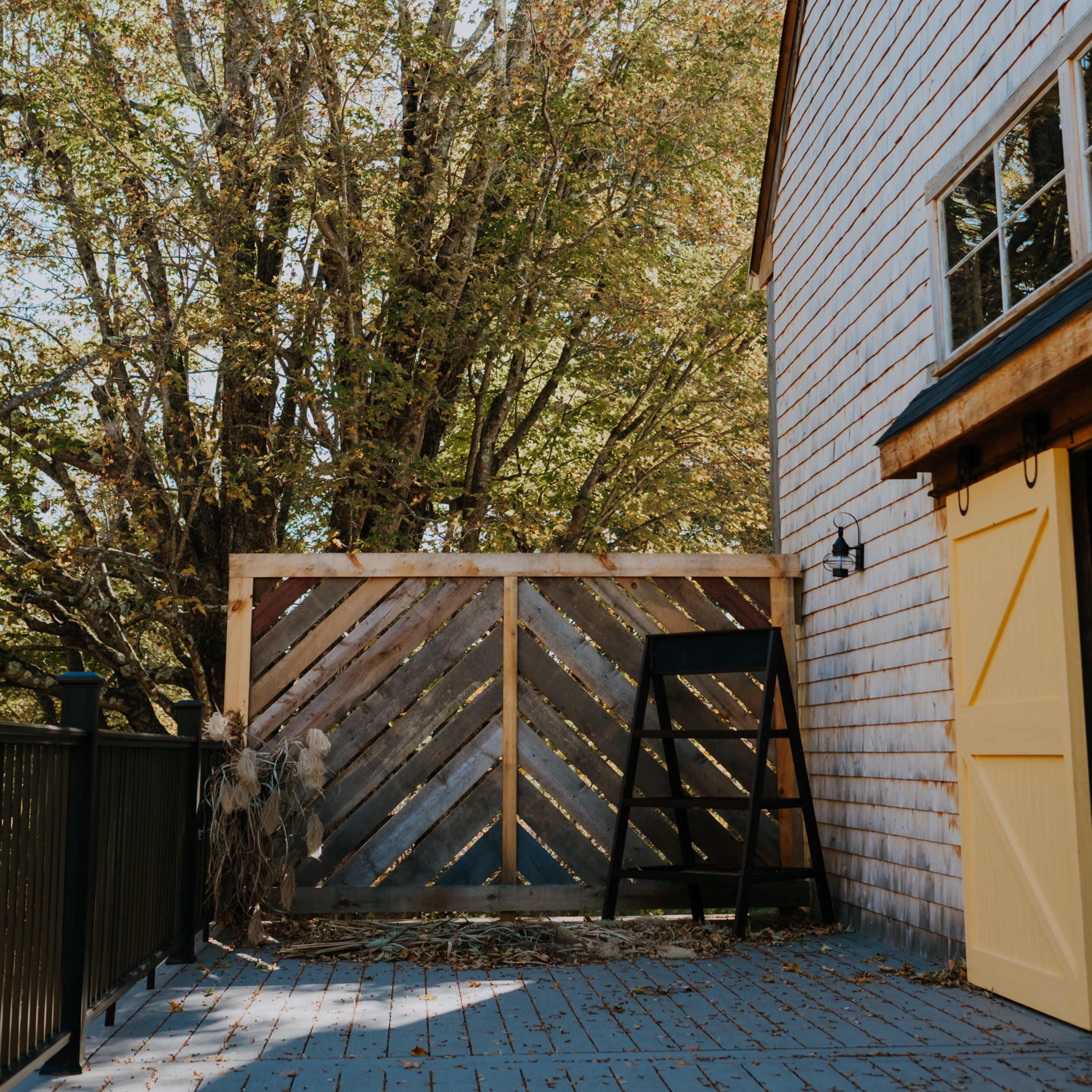 A wooden fence beside a house, with a large tree and a gray patio surface in the background.