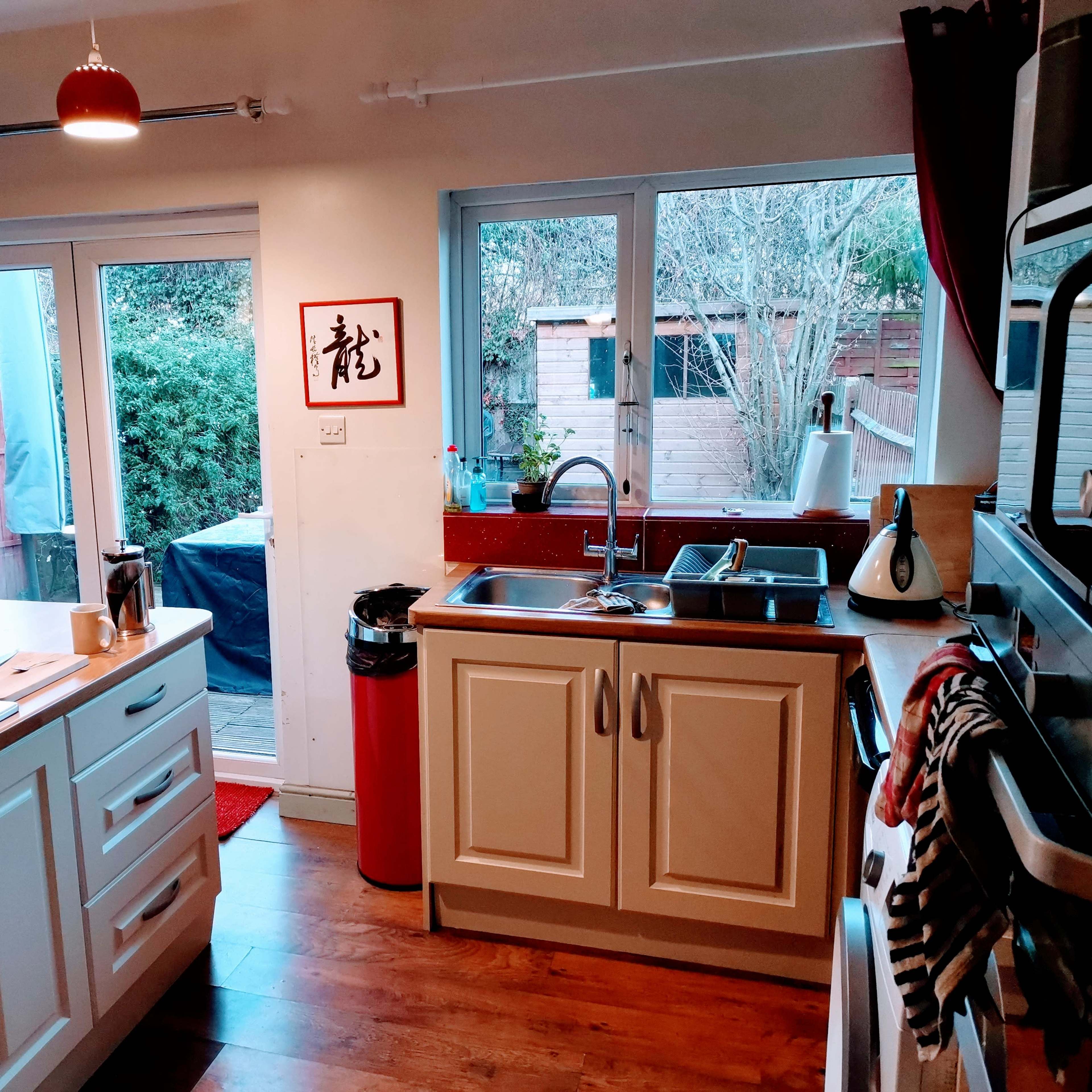 A modern kitchen with white cabinets, a sink, and large windows overlooking a backyard.