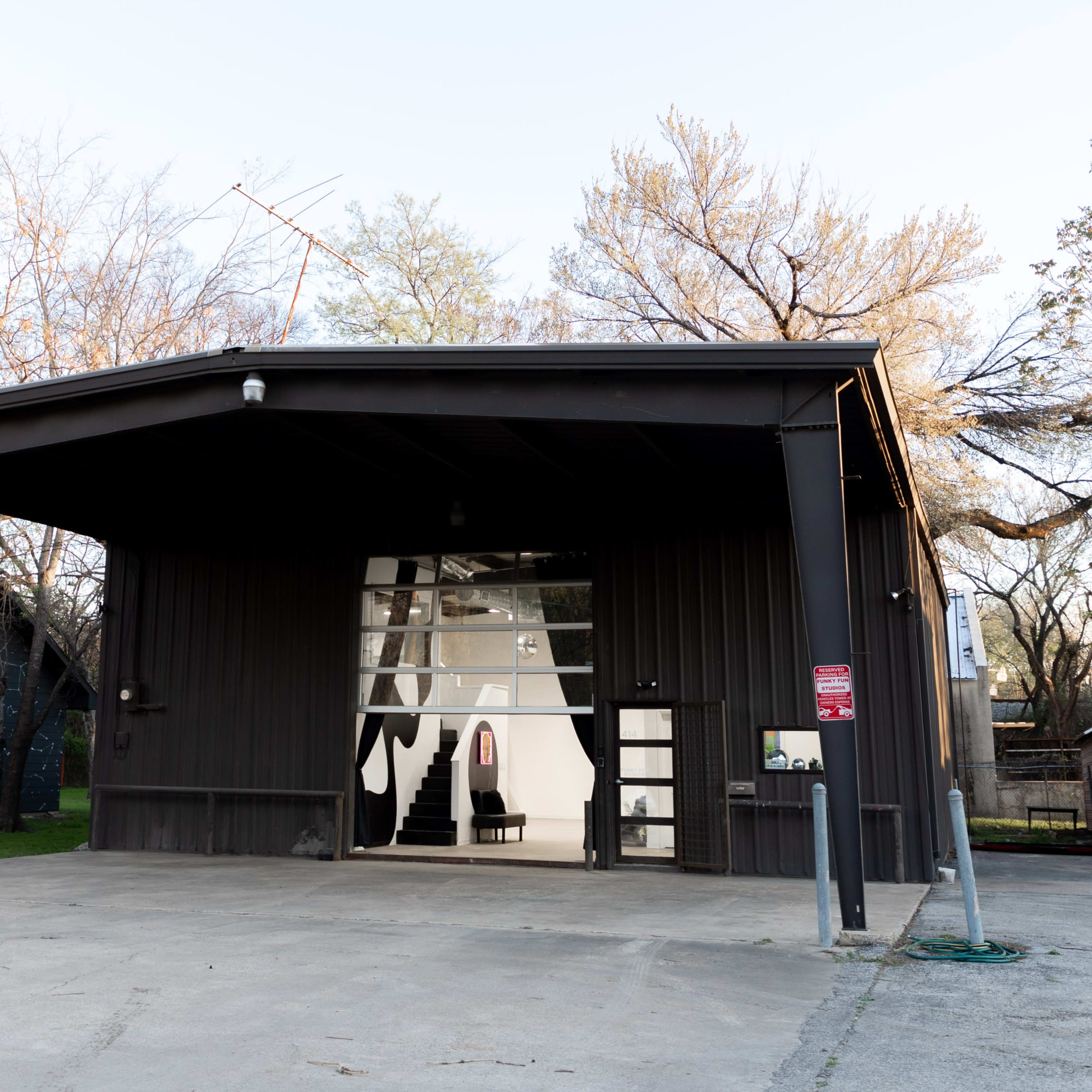 A modern black building with a flat roof, featuring large glass doors at the front and surrounded by sparse trees in a grassy area.