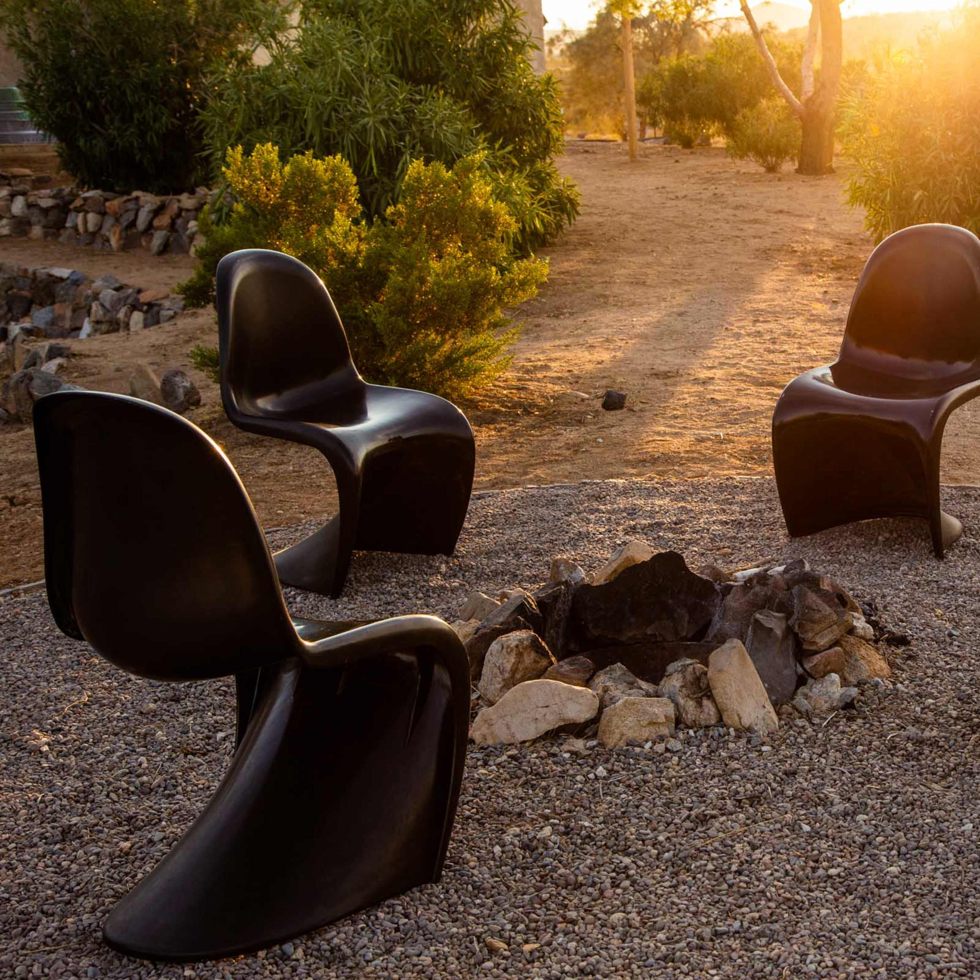 Four black chairs are arranged around a rocky fire pit in a natural outdoor setting illuminated by the sunset.