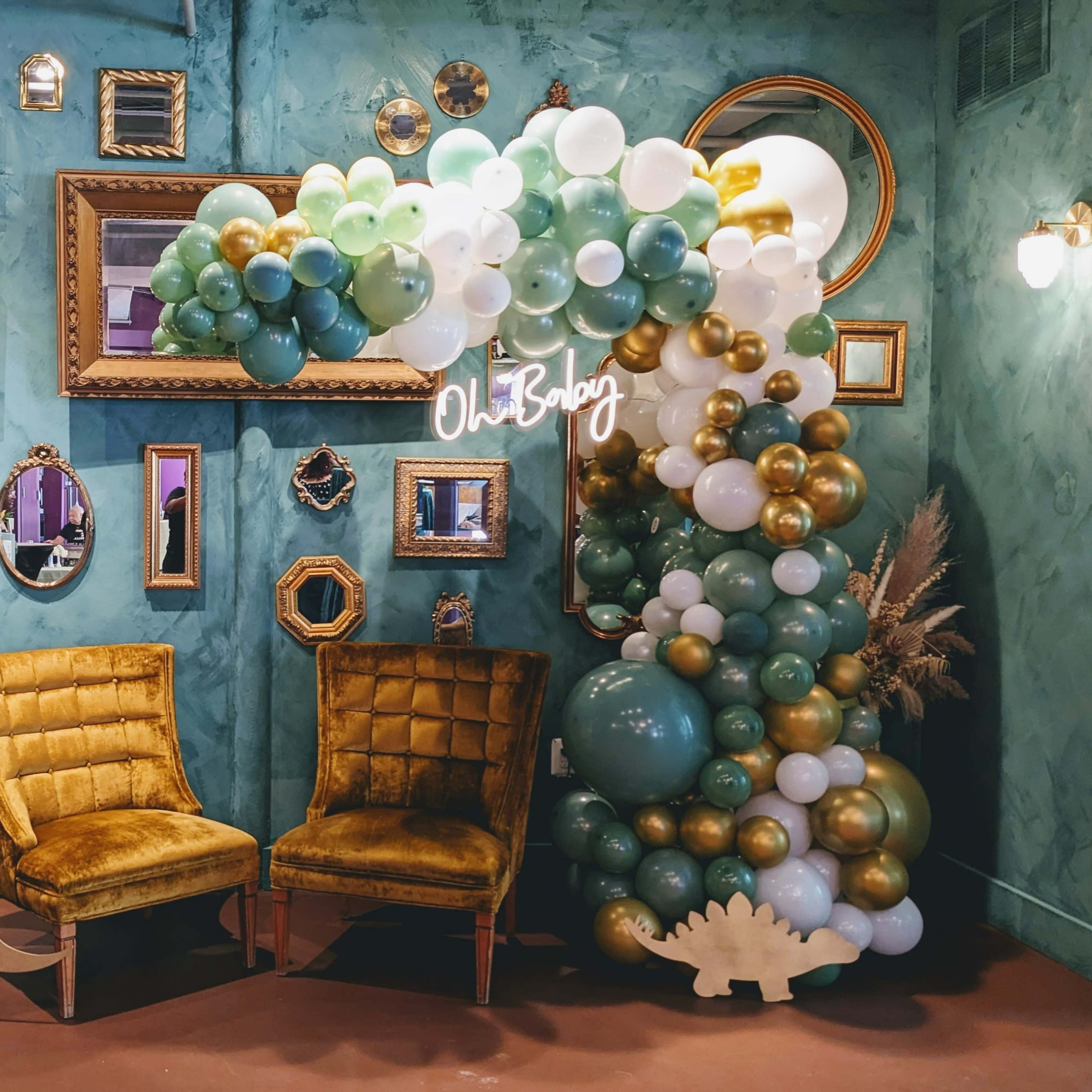 A decorated room with a balloon arch, vintage mirrors on the walls, and two yellow chairs beside decorated blocks that spell out "BABY."