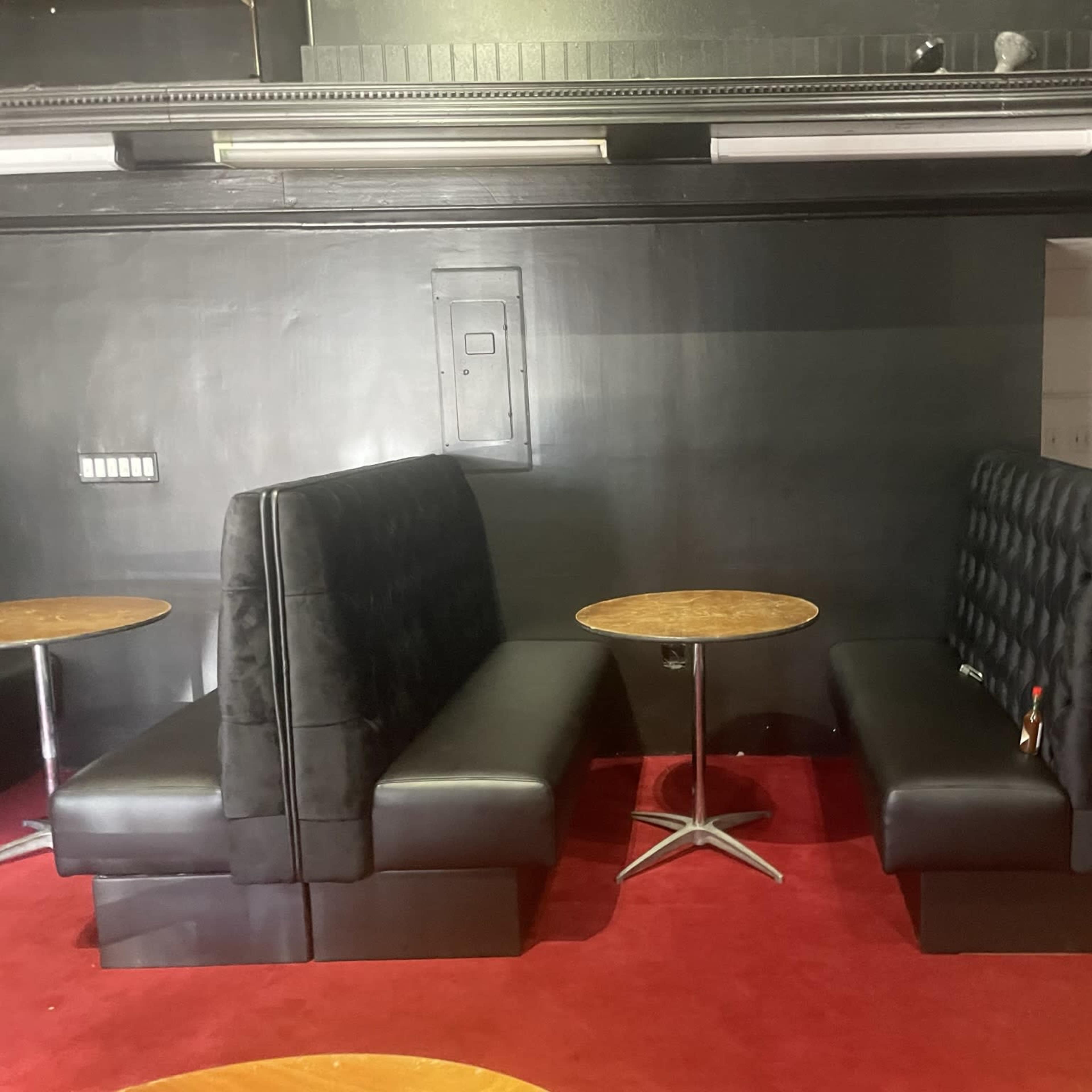 Two black leather booth seats facing each other across a small round table, set on red carpet in a dimly lit room.