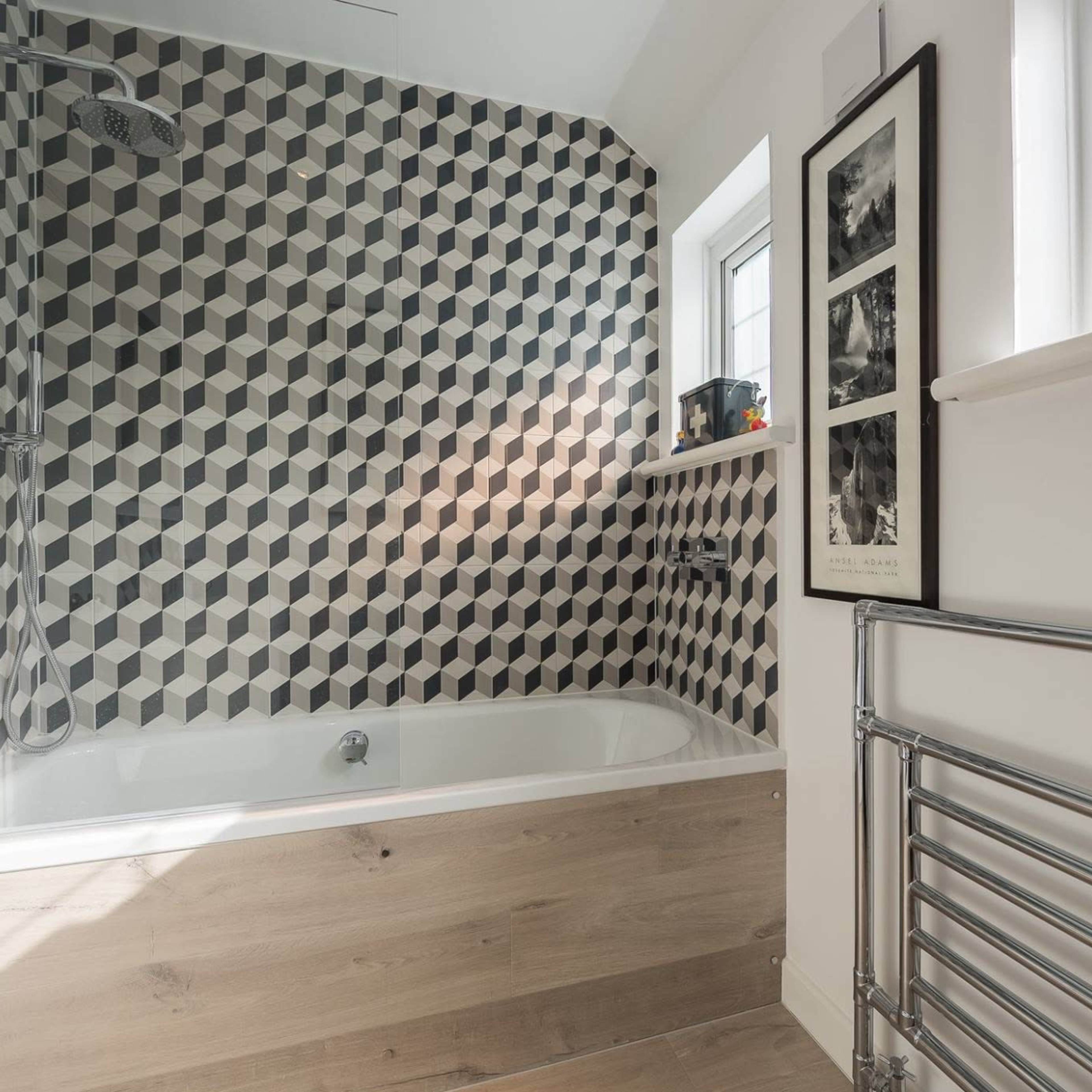 A bathroom featuring a geometric patterned wall, a bathtub, a heated towel rail, and a window allowing natural light.