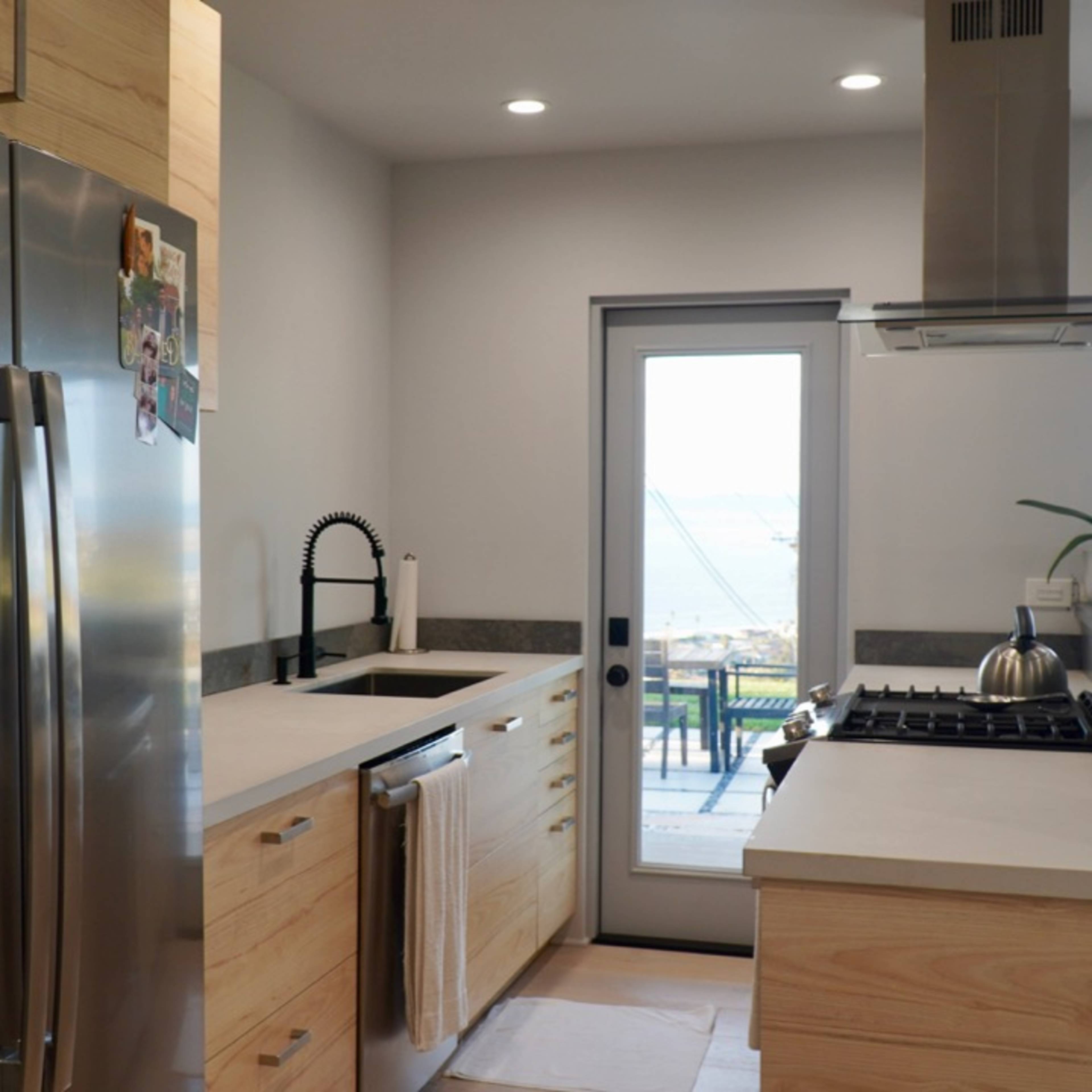 A modern kitchen featuring stainless steel appliances, wooden cabinets, and a door leading to an outdoor area.