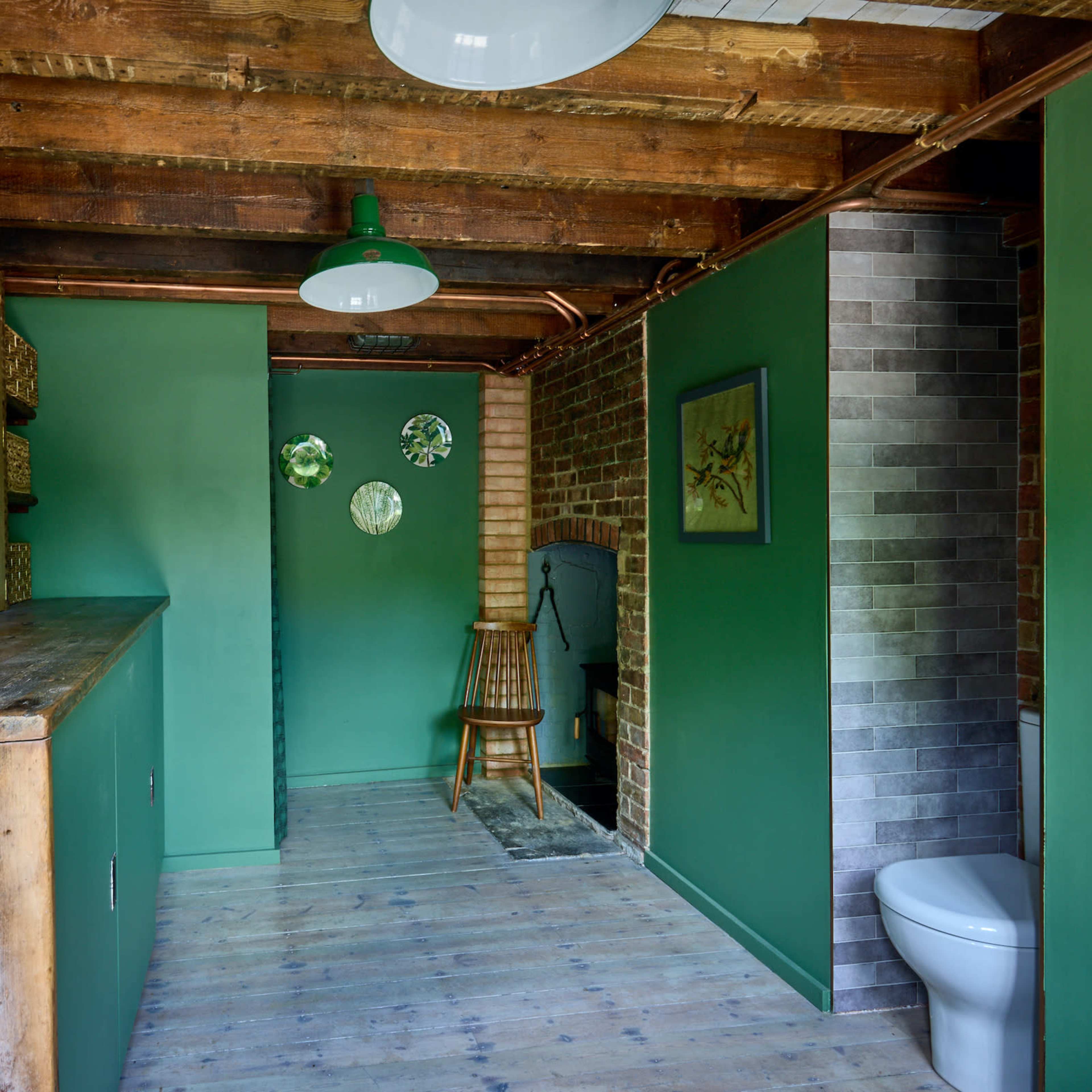 A rustic bathroom with green walls, wooden beams, a wooden countertop, and a toilet in the corner.
