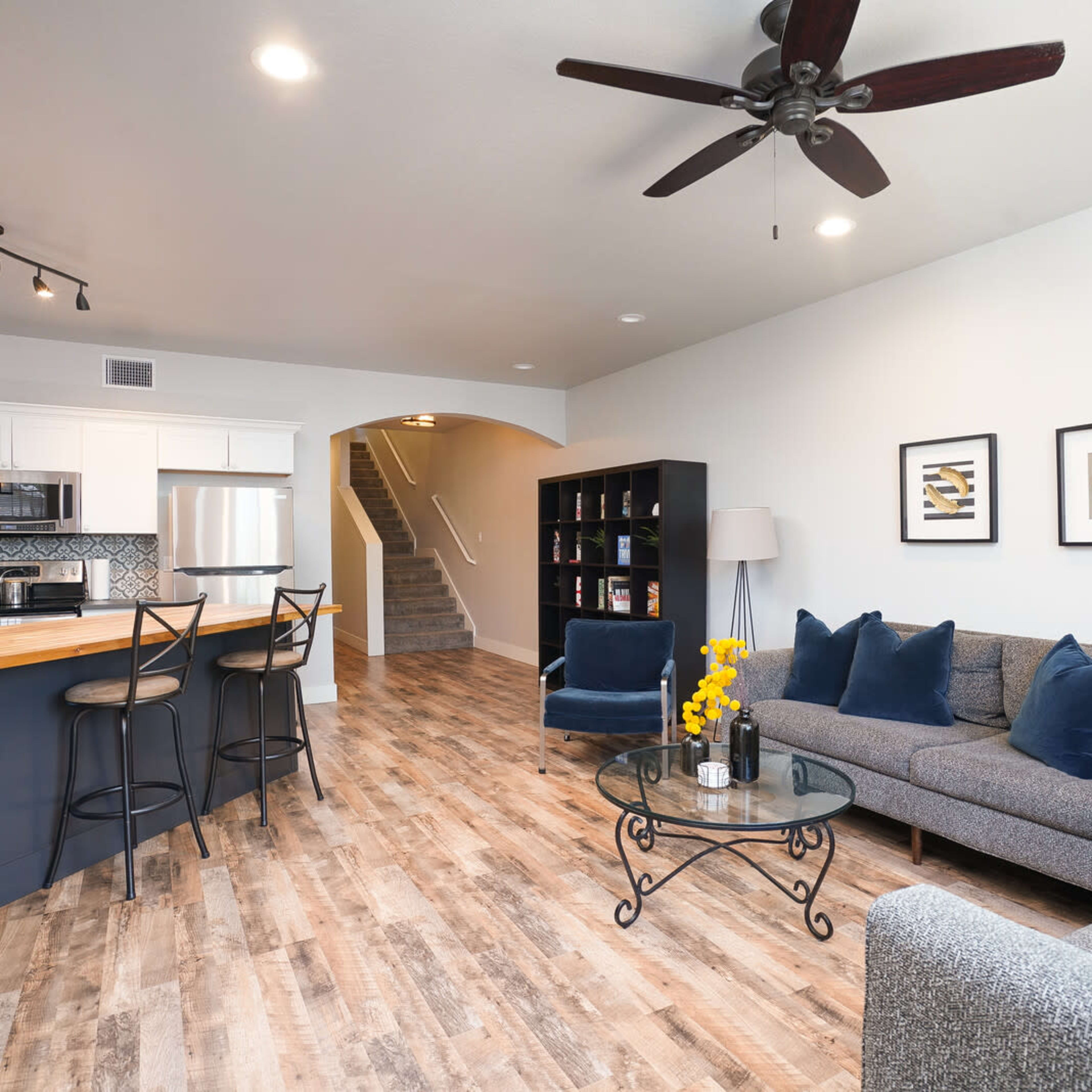 A modern living room with a gray sofa, decorative pillows, a coffee table, and a kitchen area in the background.