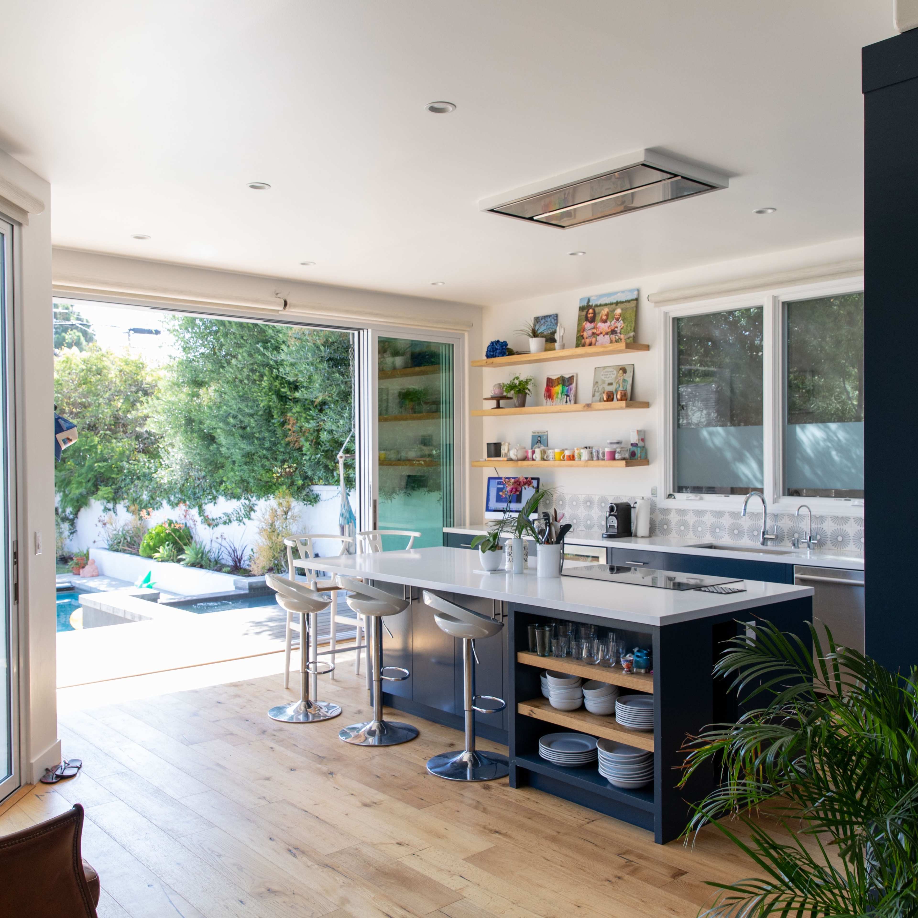 The kitchen features a modern design with a central island and bar stools, large windows opening to a patio and pool area.