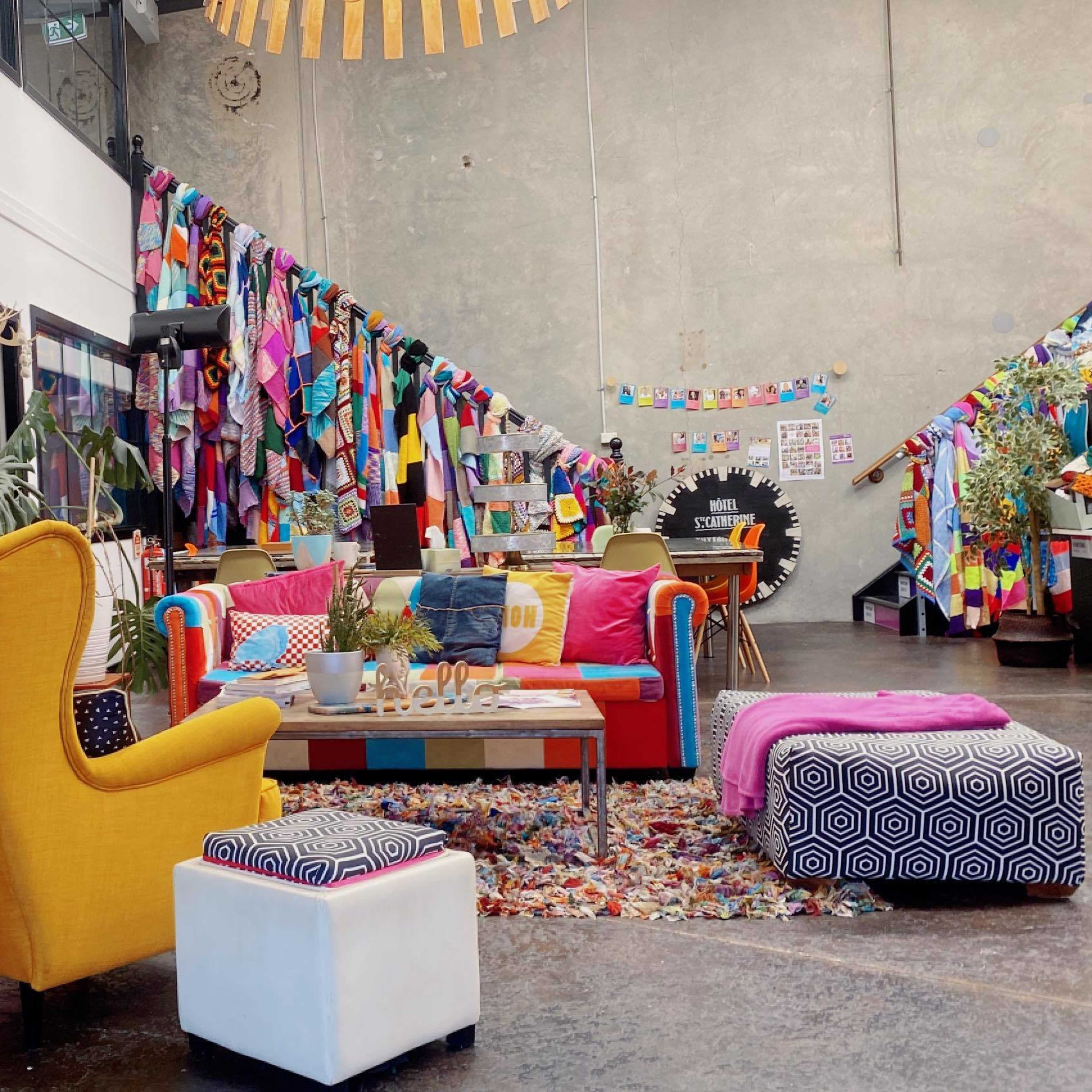 A vibrant communal space featuring colorful furniture, a bookshelf, and a wall decorated with fabric banners.