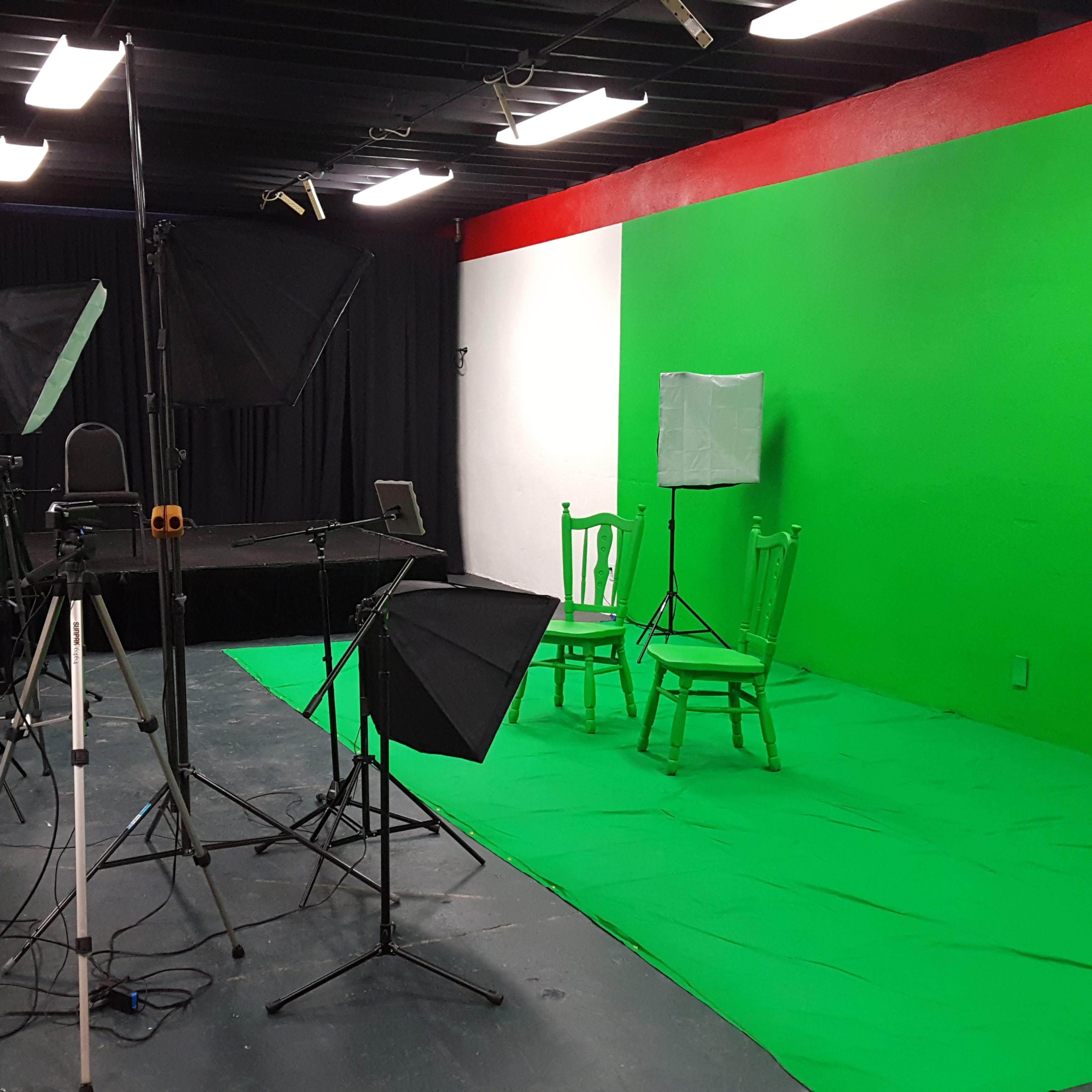 A photography studio equipped with a green screen, lighting setups, and empty chairs set against a vibrant green backdrop.