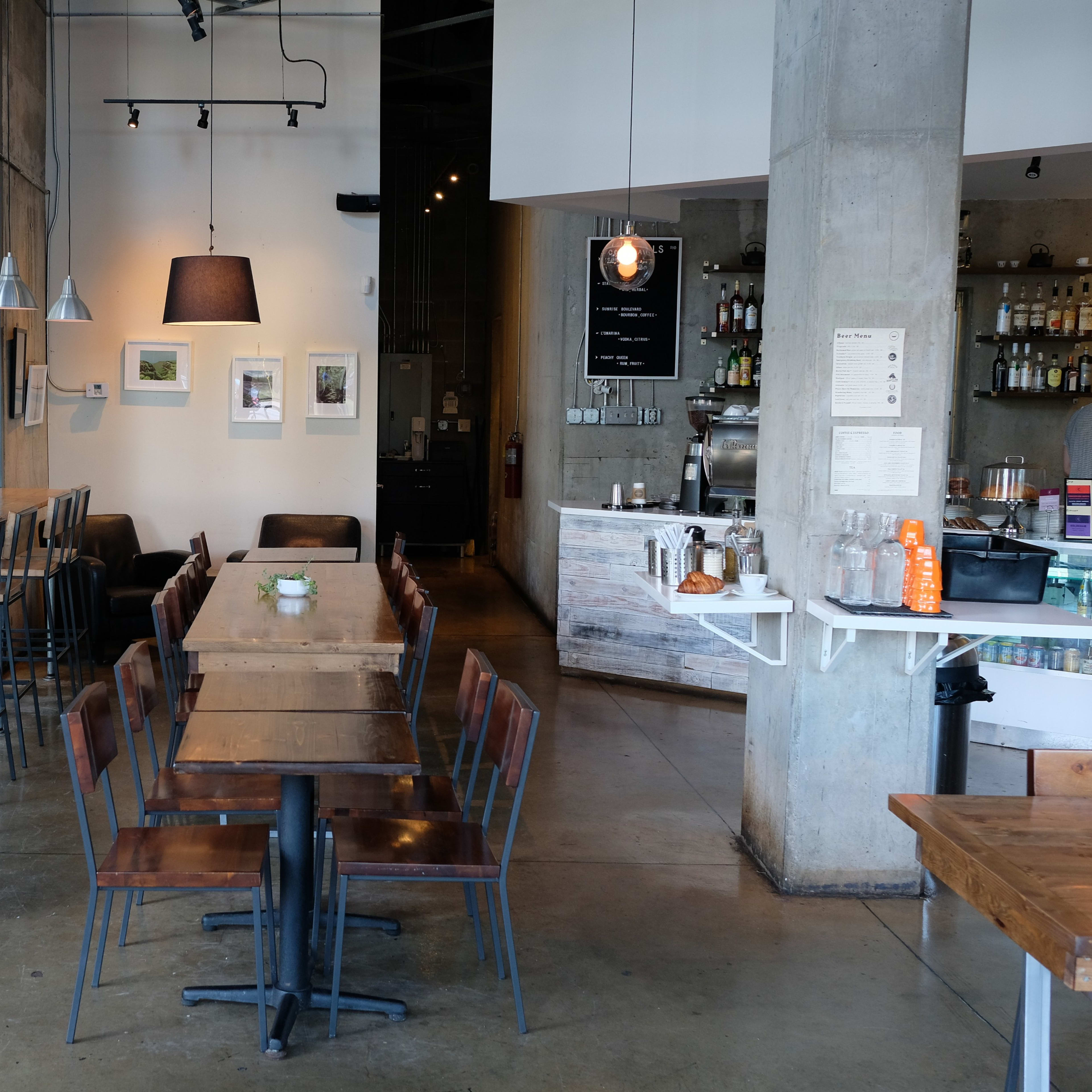 A modern café interior with a mix of high and standard seating arrangements, large windows, and a service counter in the background.