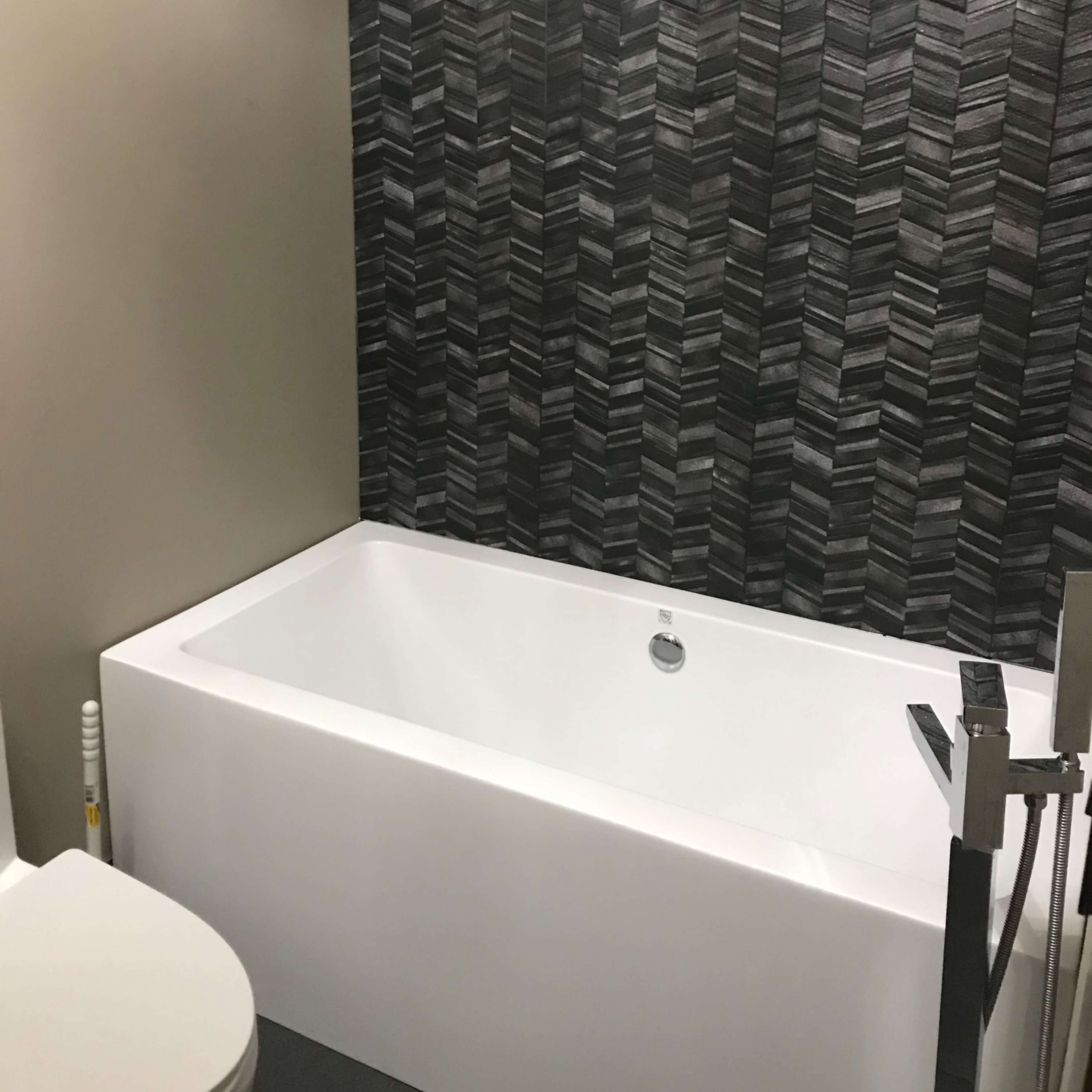 A bathroom featuring a white bathtub adjacent to a toilet, with a geometric patterned black and gray wall in the background.