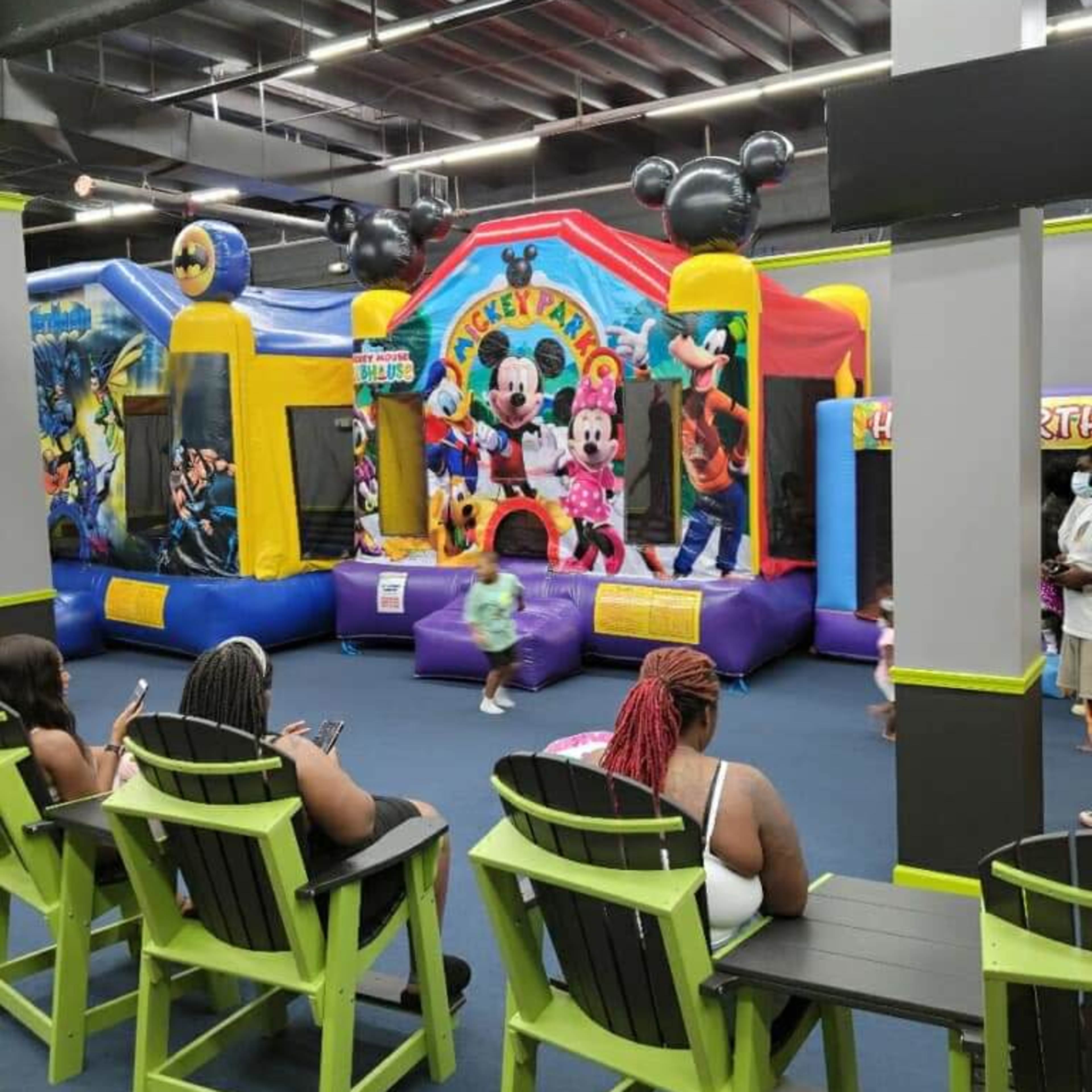 Several colorful bounce houses in a playground area, with children playing inside while adults sit on chairs nearby.