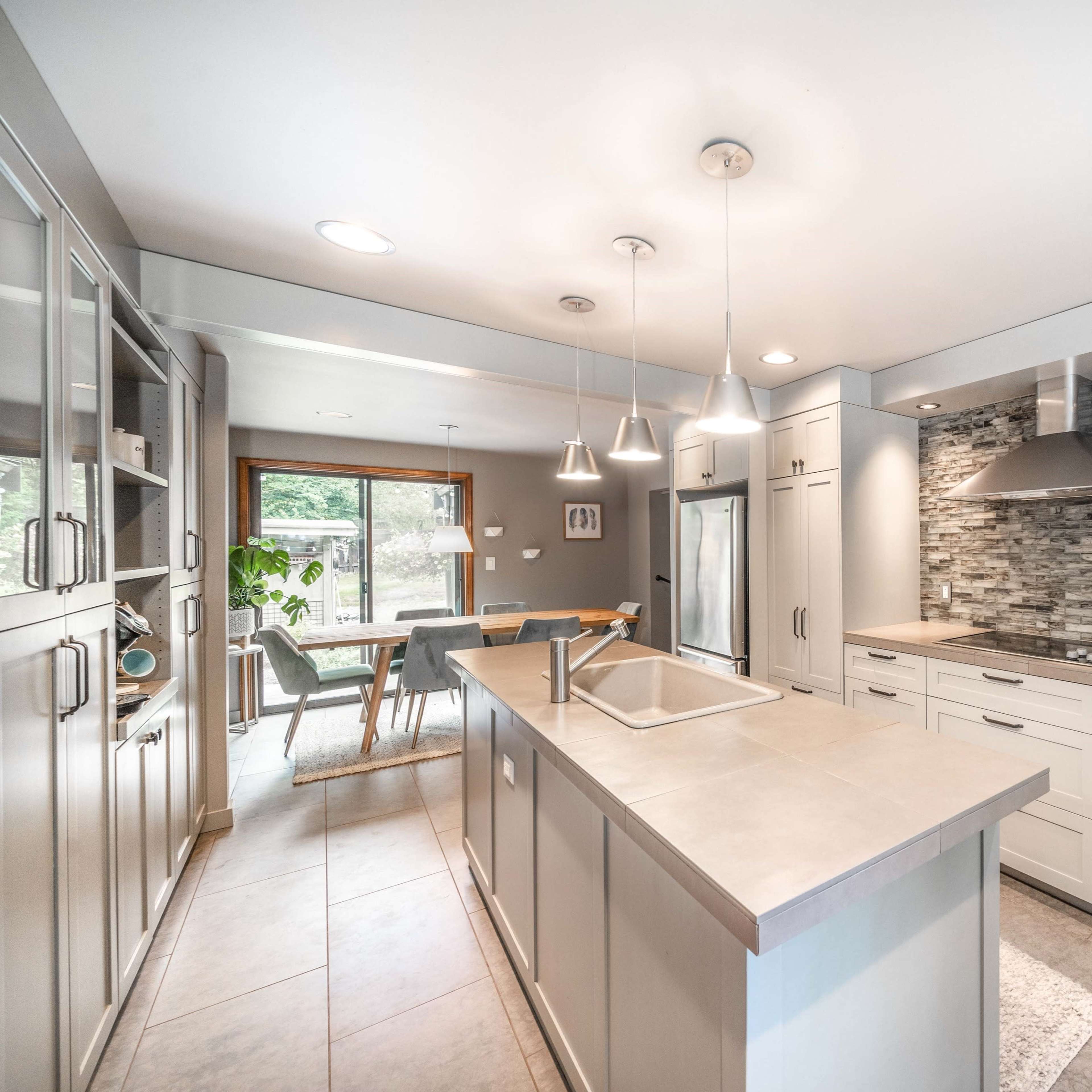 A modern kitchen with light cabinetry, a central island, and stainless steel appliances, featuring a textured stone backsplash.