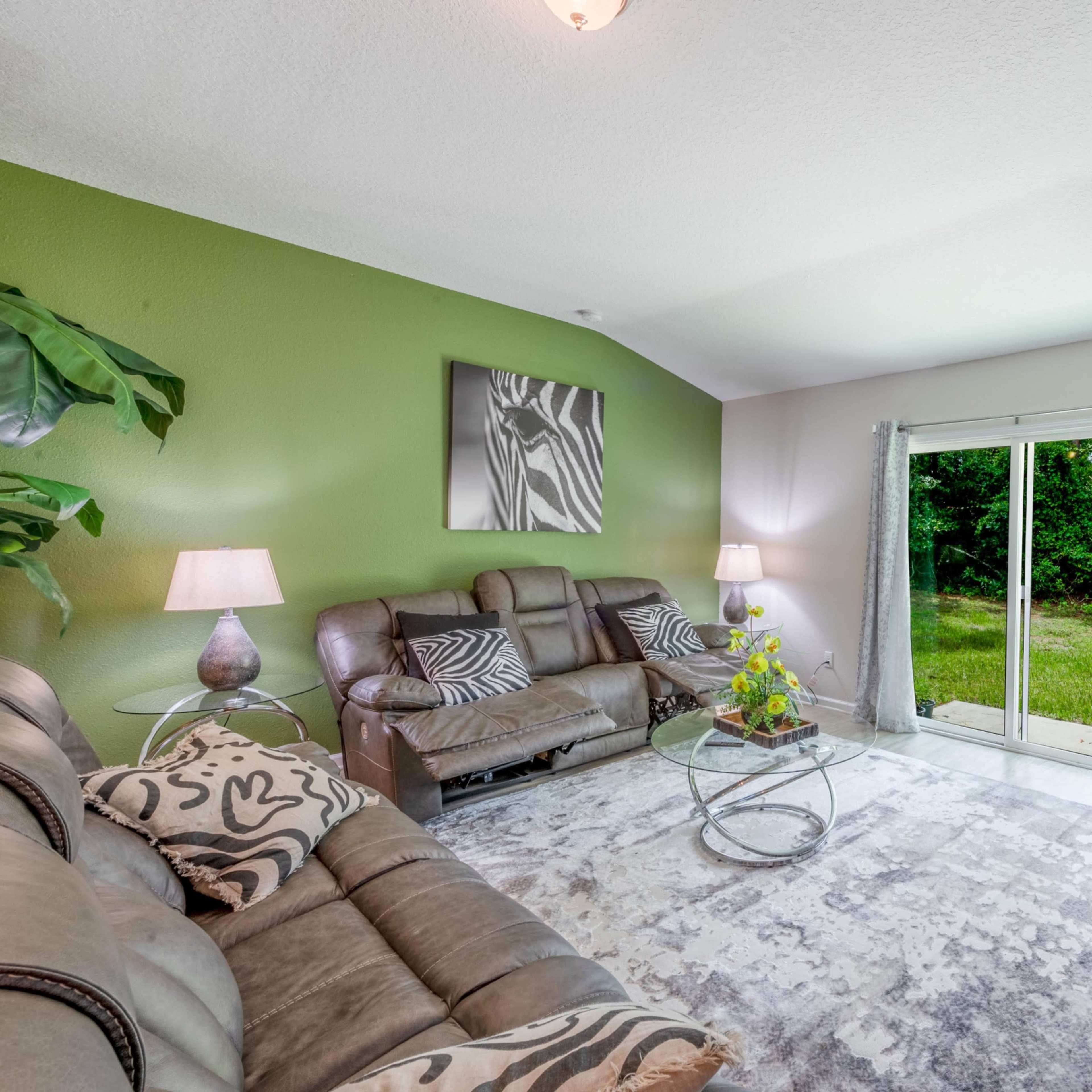 A living room with two leather sofas, a coffee table, and sliding glass doors leading to a grassy outdoor area.
