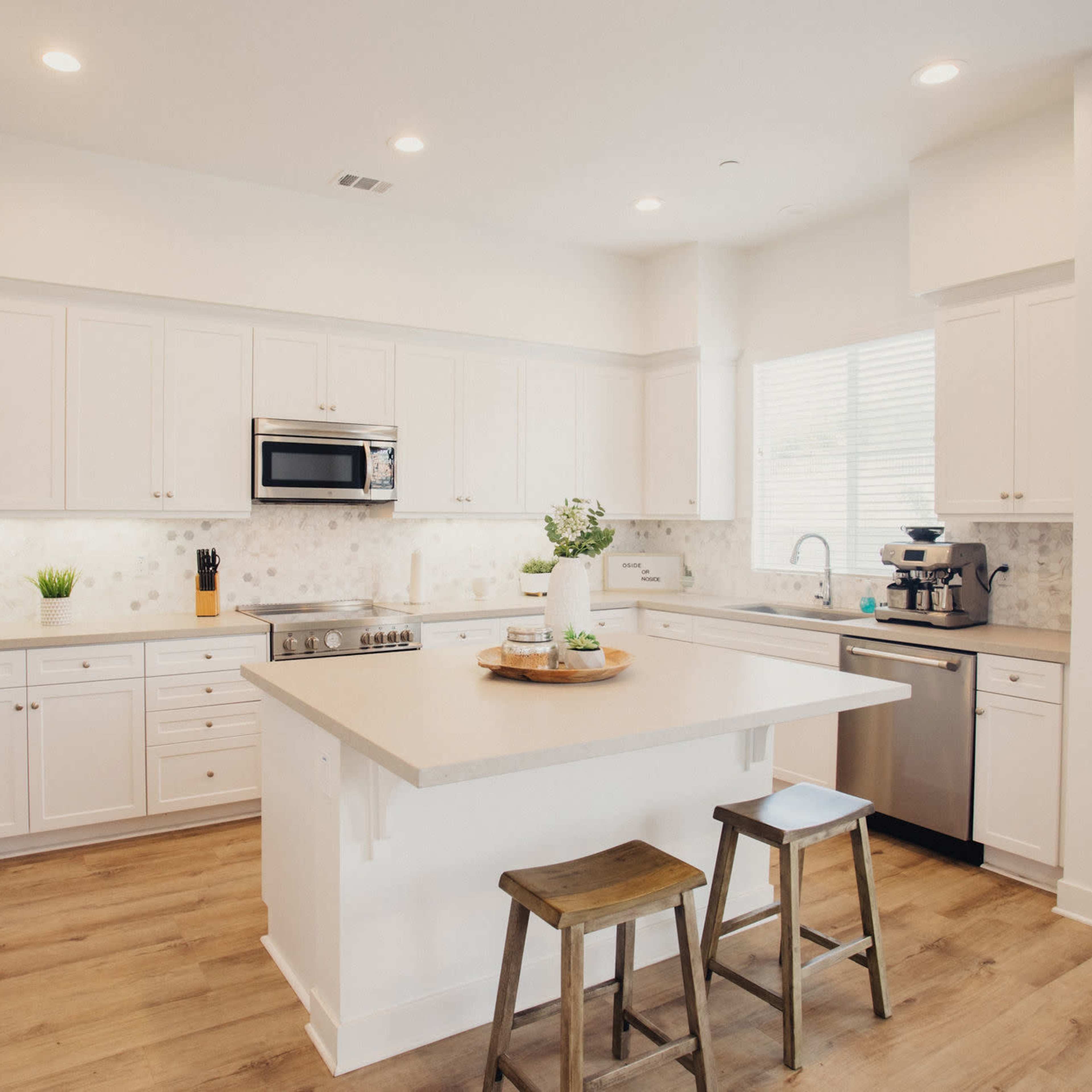 The kitchen features white cabinetry, stainless steel appliances, and a central island with two wooden stools.