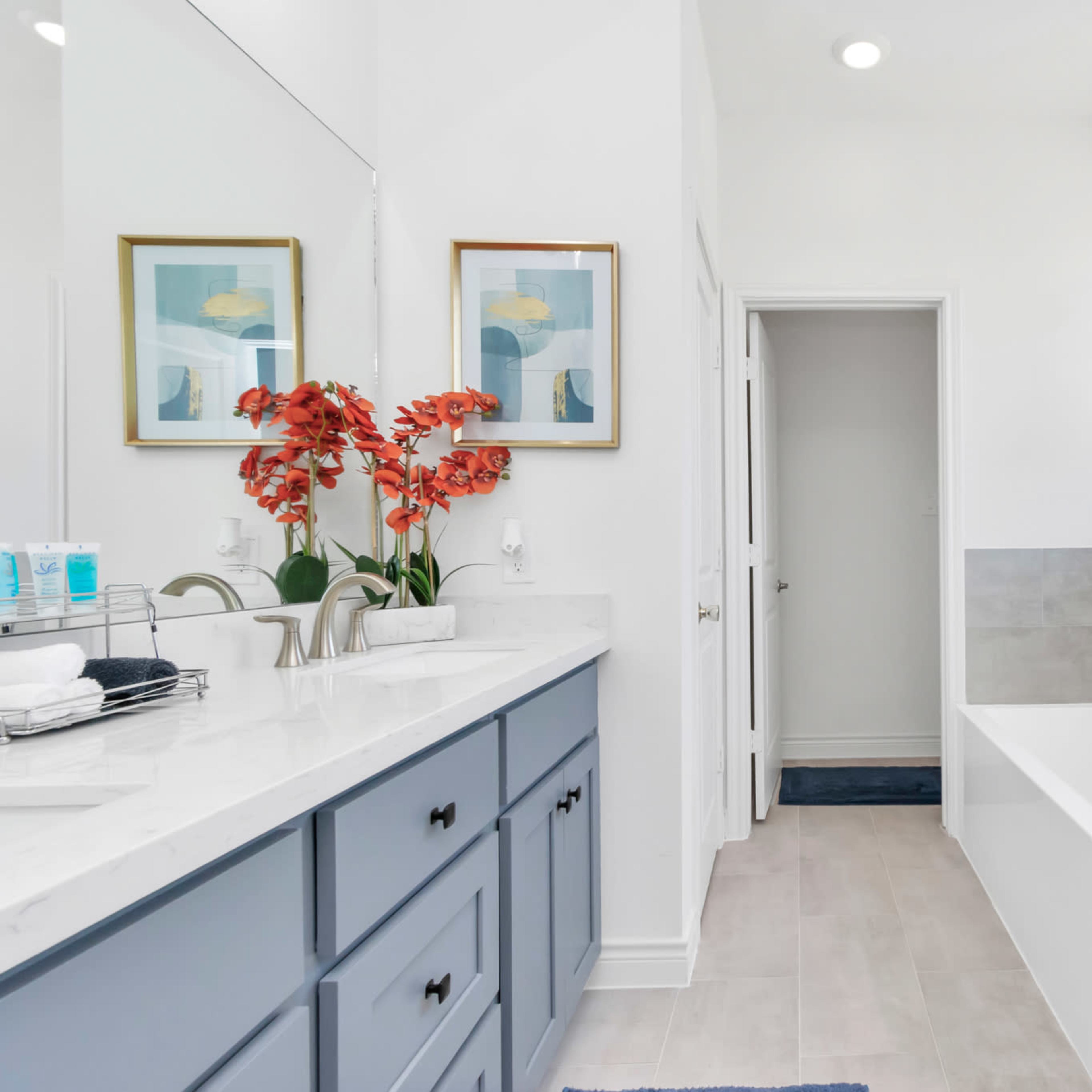 A modern bathroom featuring a double vanity with blue cabinets, a white countertop, and a glass-enclosed shower beside a freestanding bathtub.