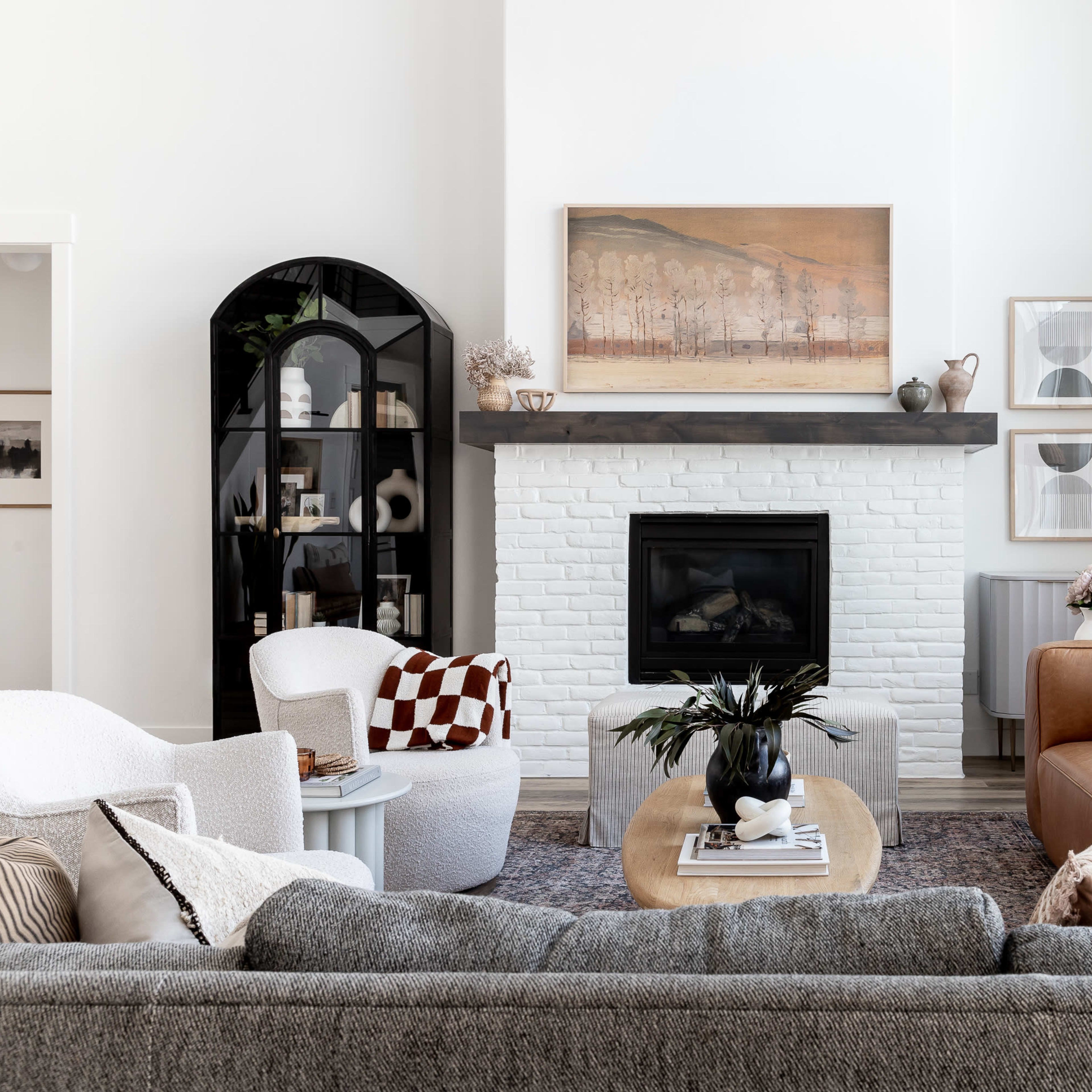 A spacious living room features a white-brick fireplace with a mounted artwork above it, surrounded by various seating options and a coffee table.