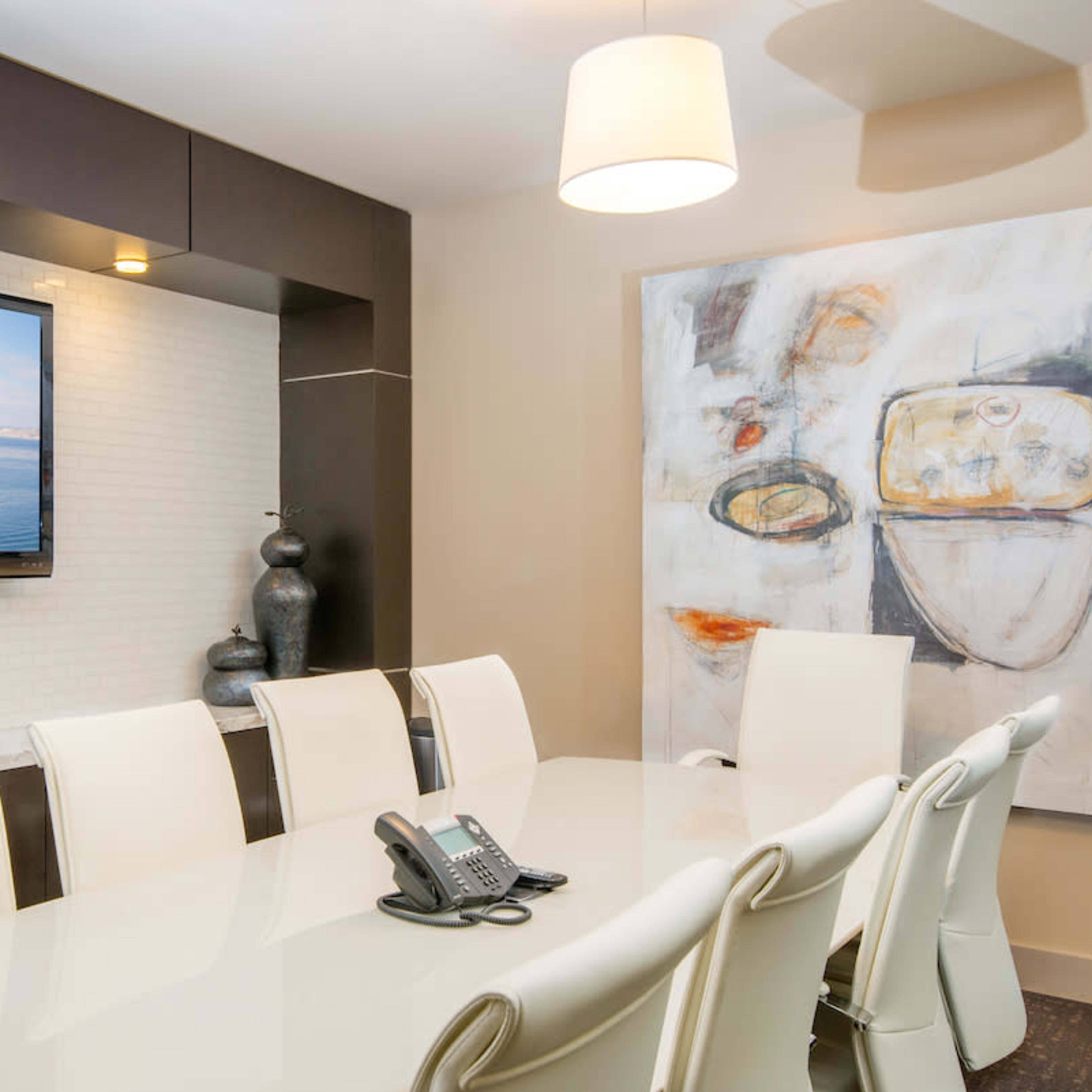 A modern conference room with a large table, white chairs, a television mounted on the wall, and an abstract painting beside it.