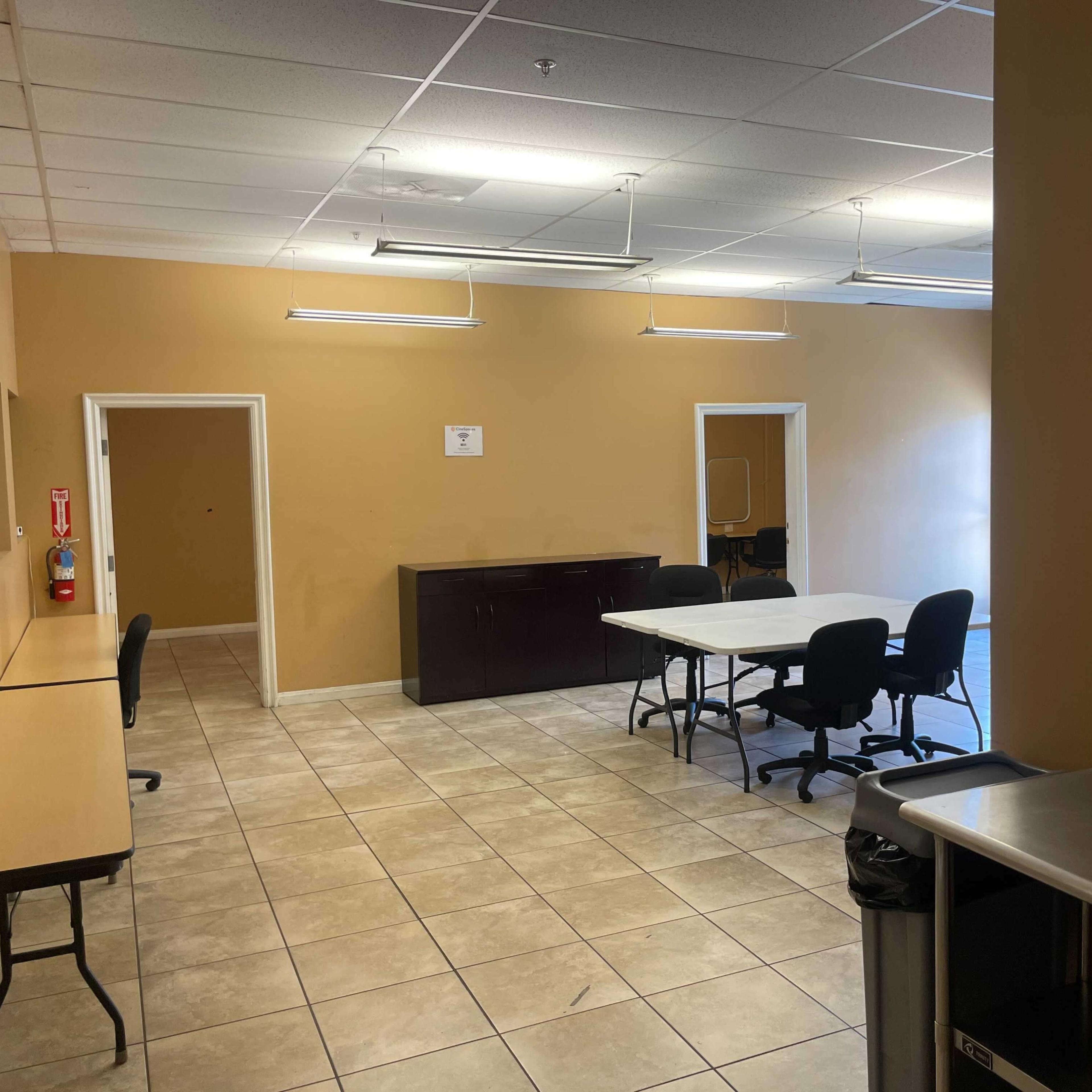 An empty breakroom with several tables and chairs, a coffee machine, and areas for storage along the walls.