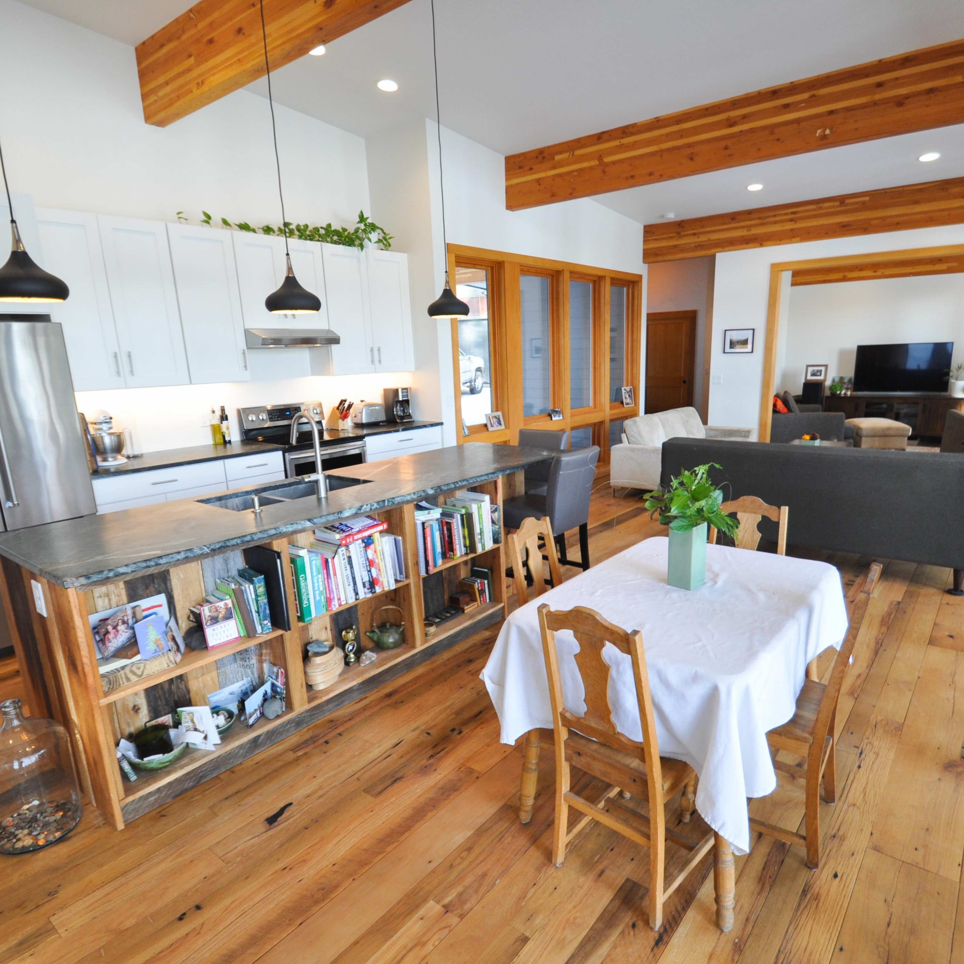 A modern open-concept kitchen and living area with wooden beams, a central table, and a cozy seating arrangement.