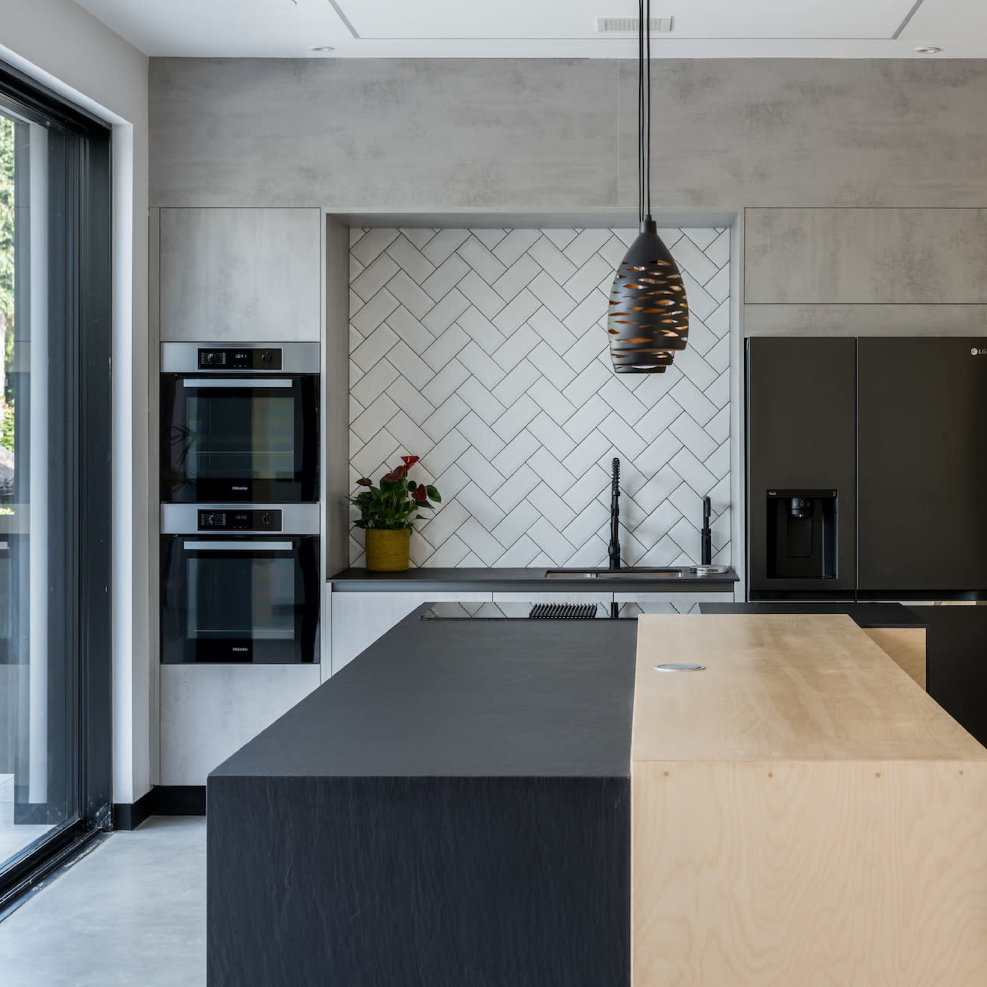 A modern kitchen featuring a large island with a black countertop, built-in appliances, and a geometric tile backsplash.