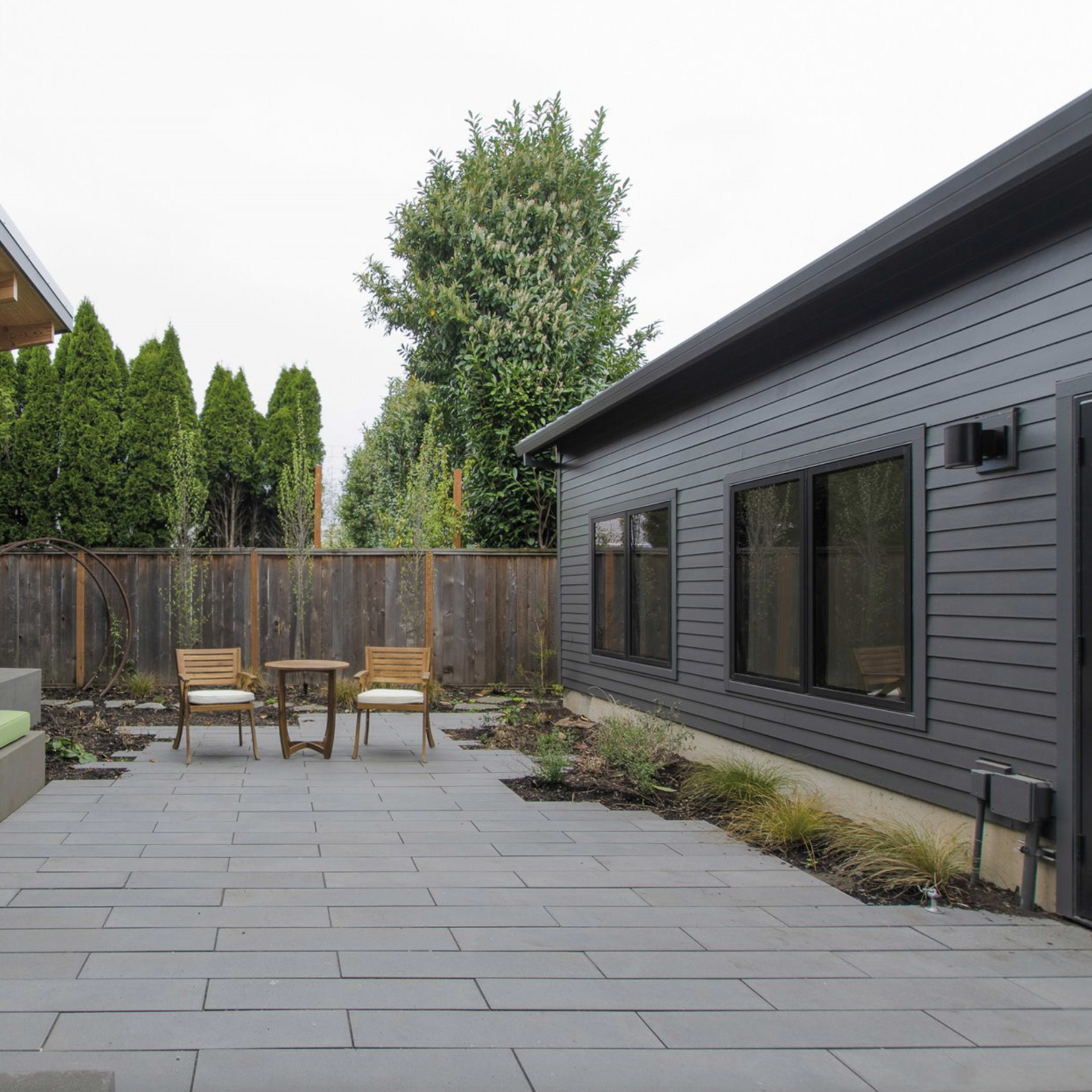 A paved courtyard between two modern buildings featuring a green cushioned seating area and two wooden chairs.