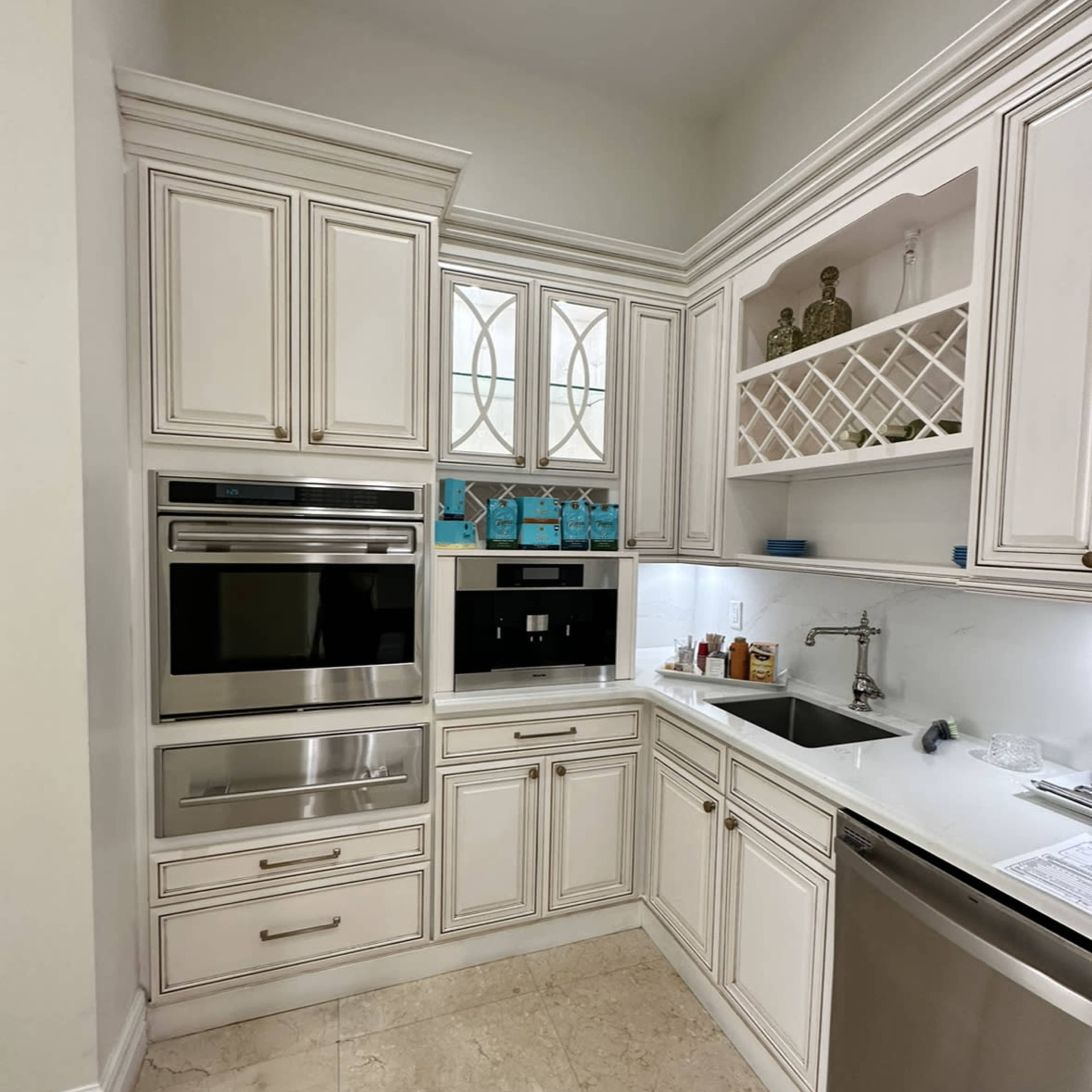 A modern kitchen with white cabinetry, built-in appliances, and a marble-tiled floor.