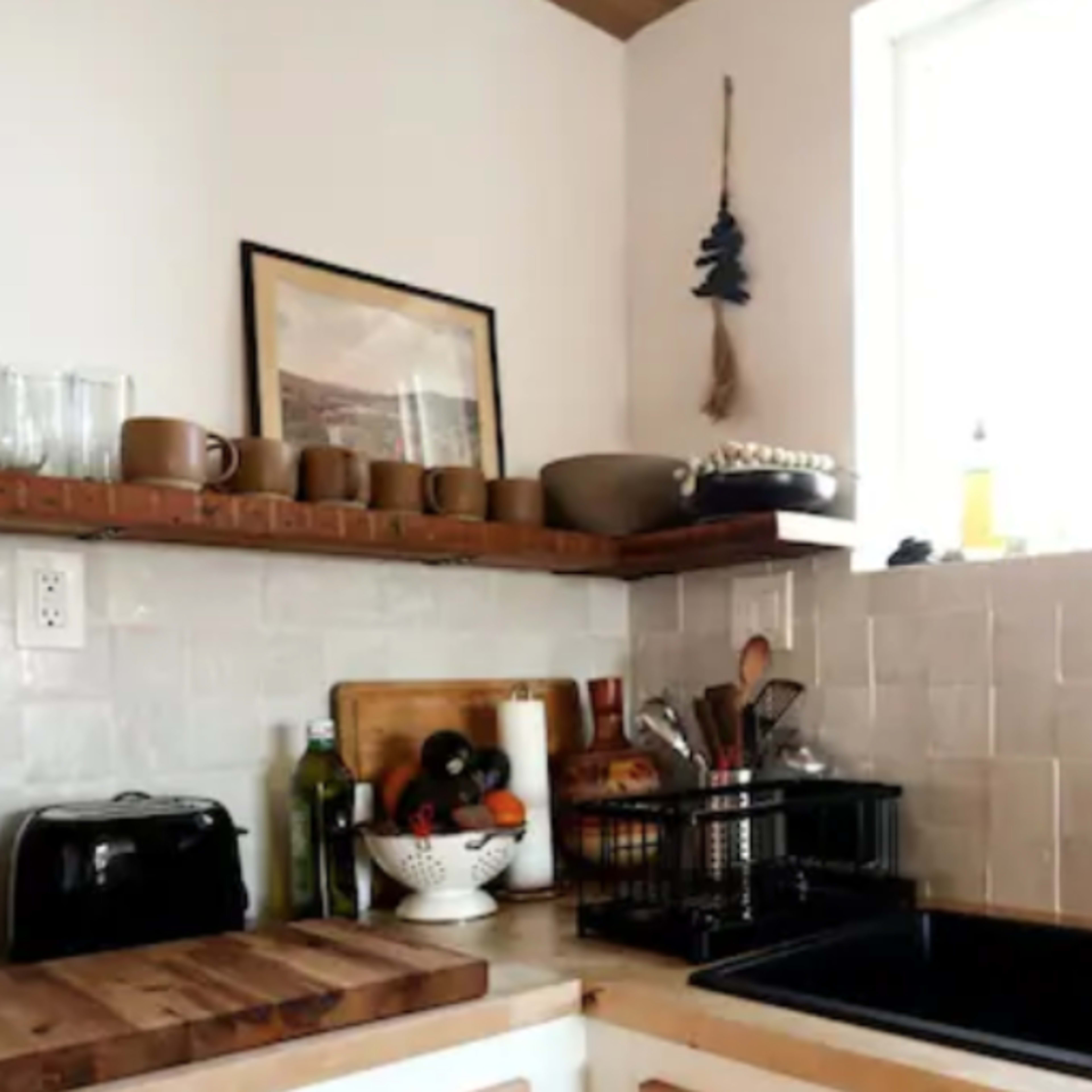 A modern kitchen with wooden shelves, a black sink, and various kitchen utensils and decor arranged on the countertops.