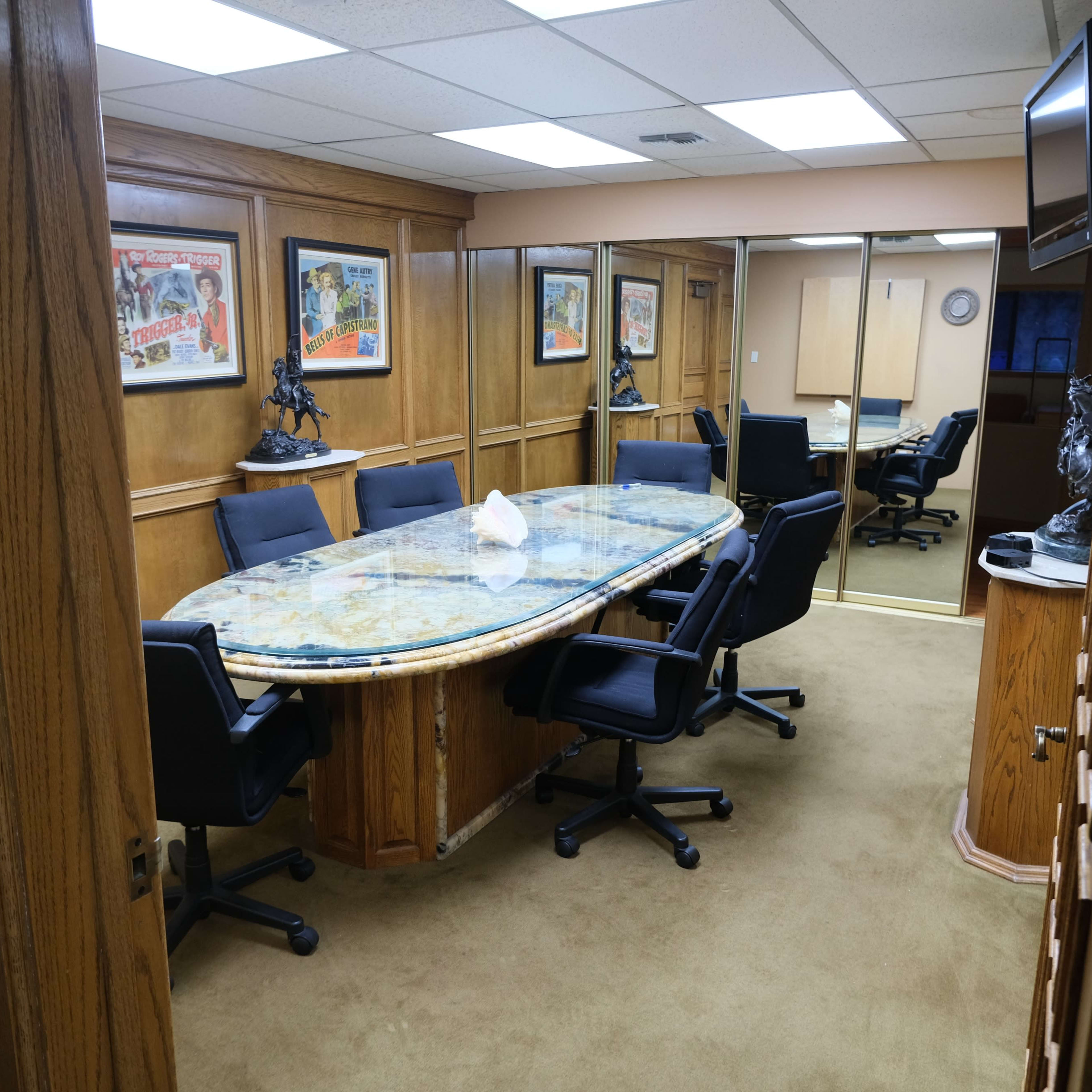A wooden conference room with a large oval table surrounded by black chairs, decorated with framed posters on the walls.