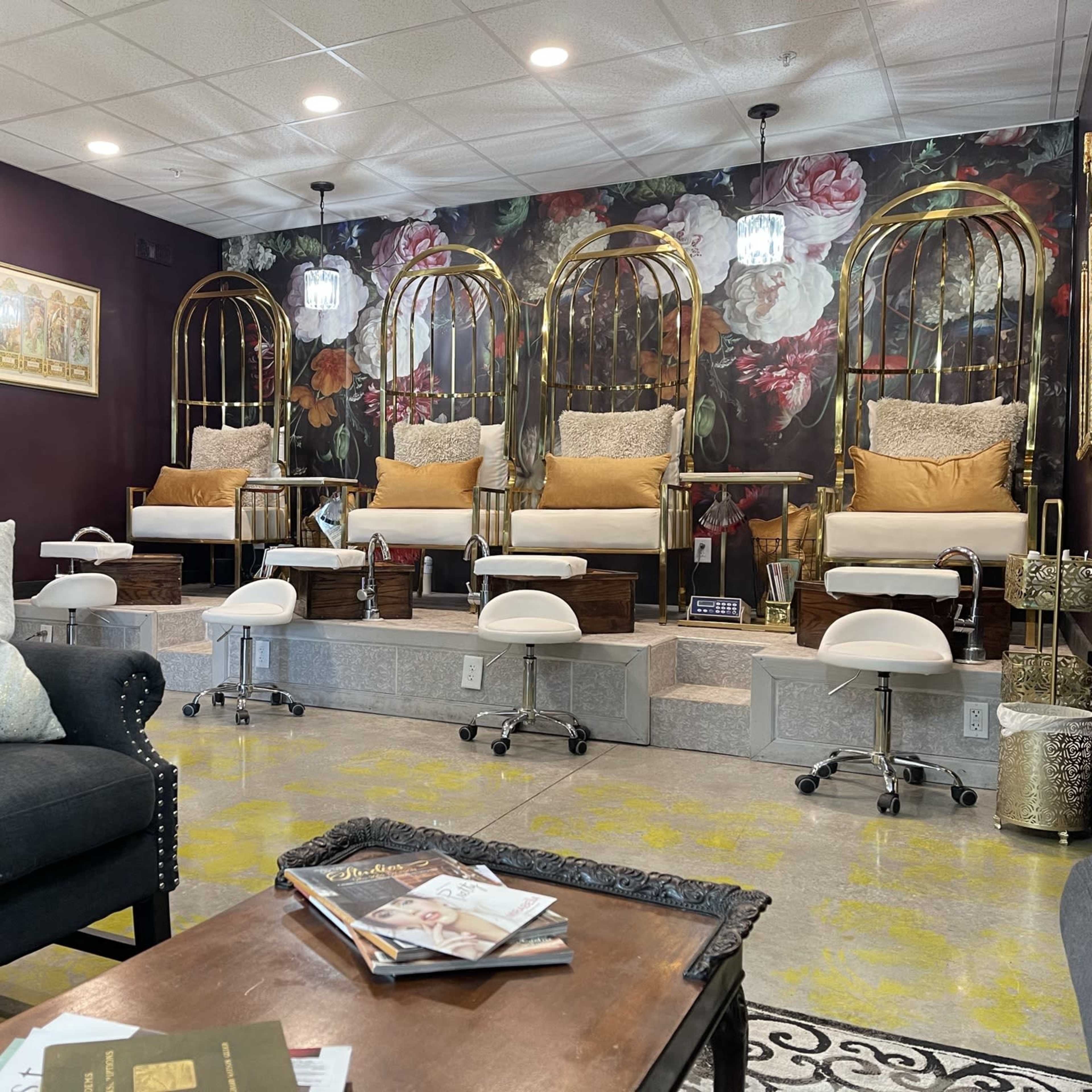 A nail salon interior featuring four manicure stations with cushioned seating and decorative floral wallpaper in a dimly lit setting.