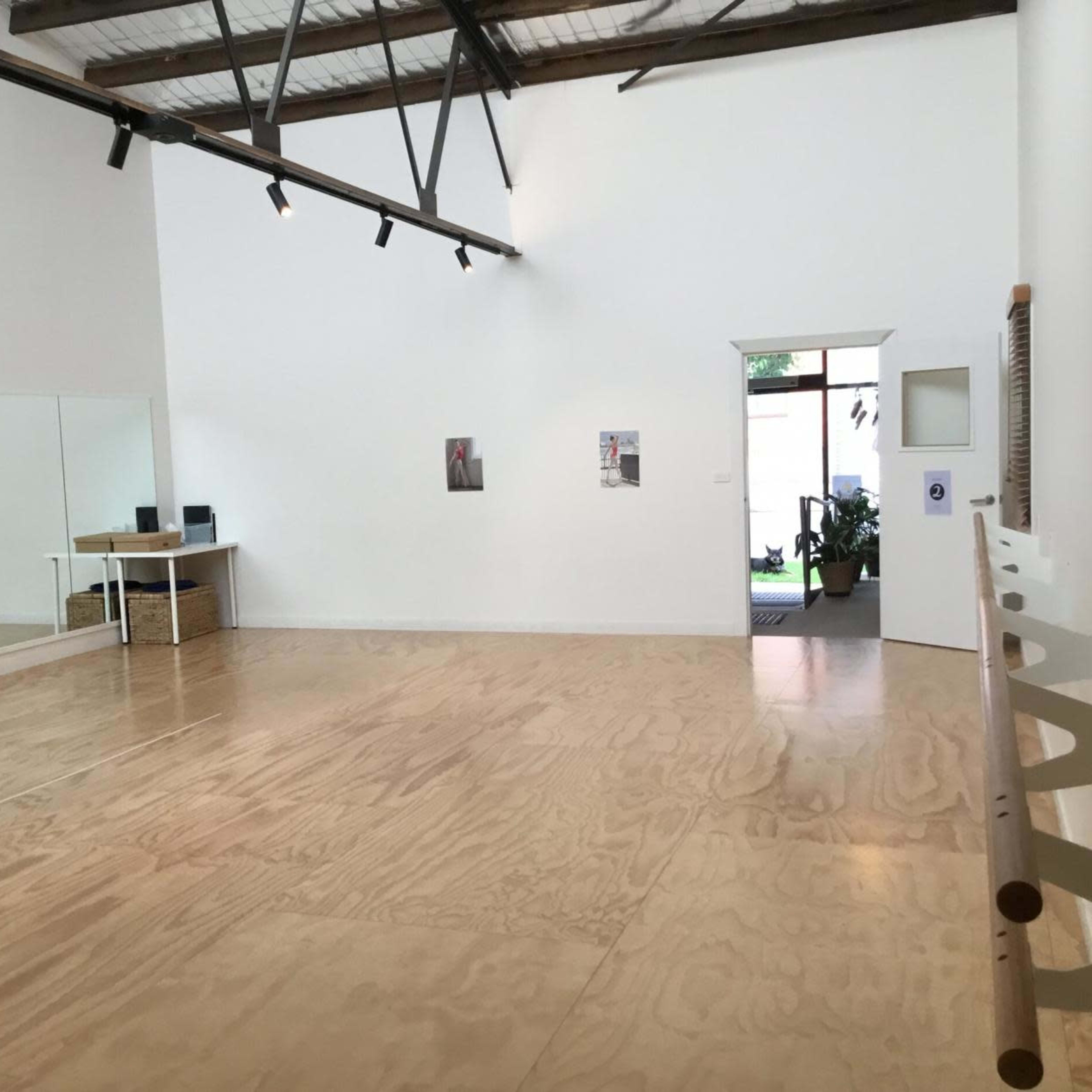 An interior room features a wooden floor, a large mirror on one wall, and a doorway leading to an outdoor area.