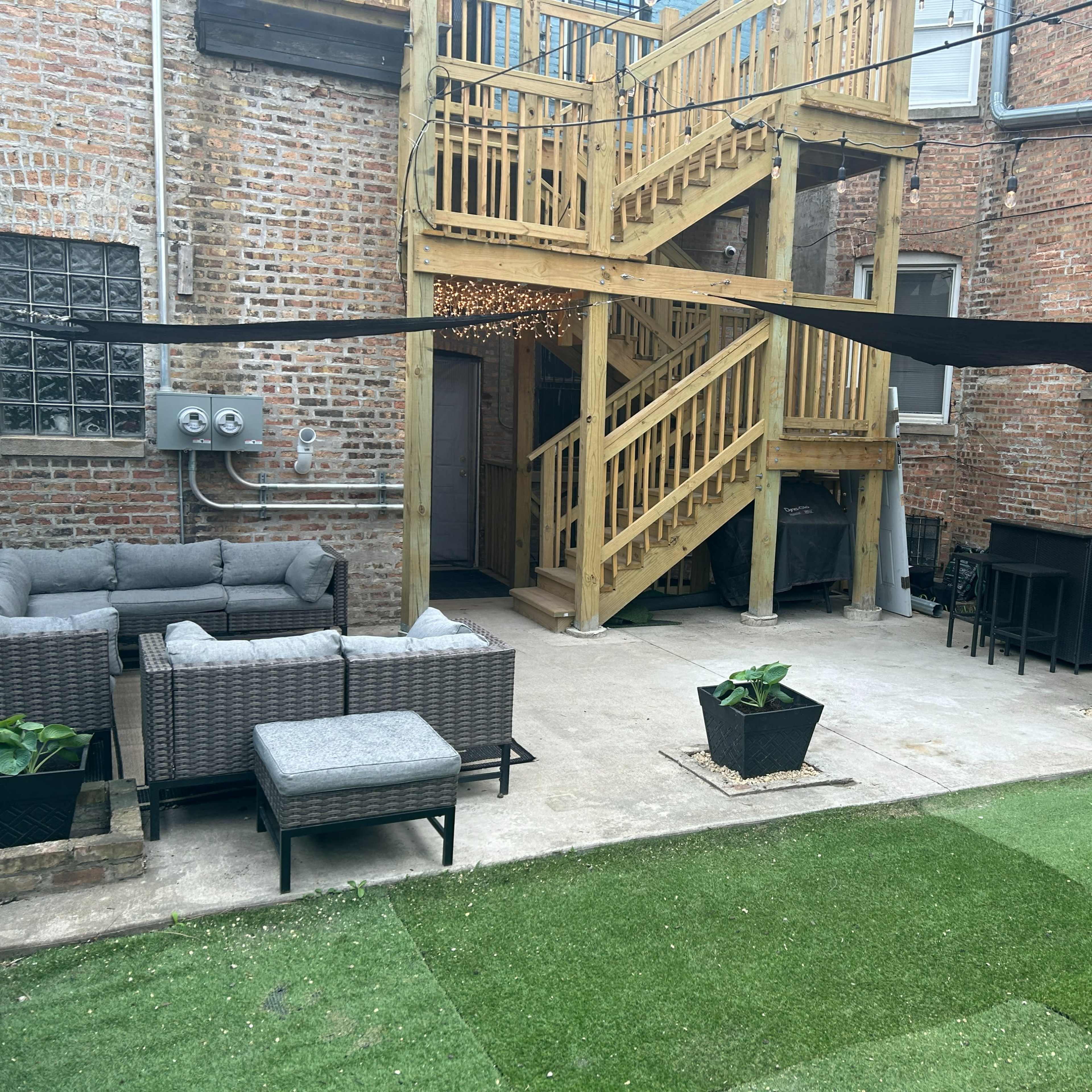 A fenced backyard area featuring a wooden staircase, outdoor furniture, and a lawn with artificial grass.