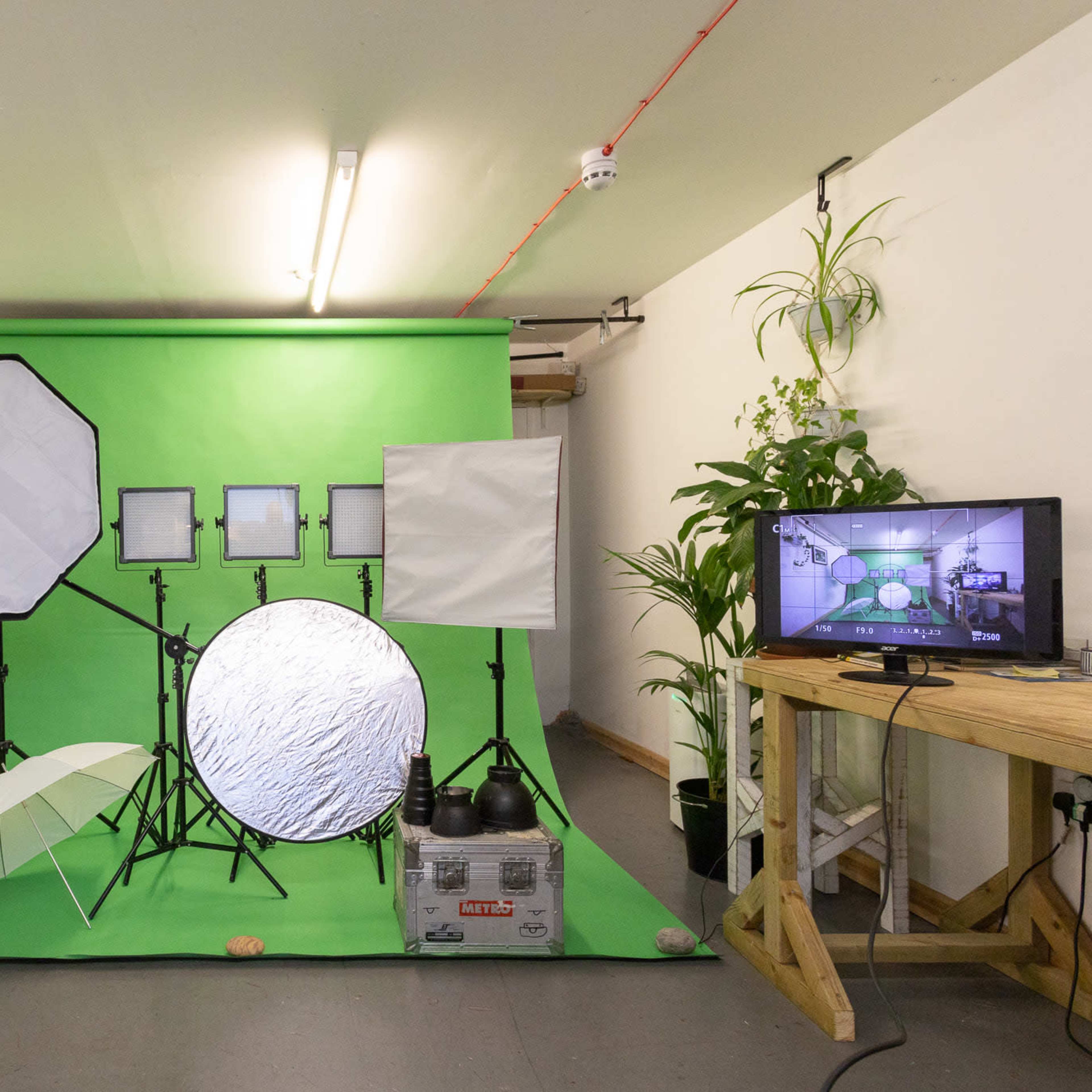 A photography studio setup featuring a green backdrop, various lighting equipment, and a television monitor displaying a camera feed.