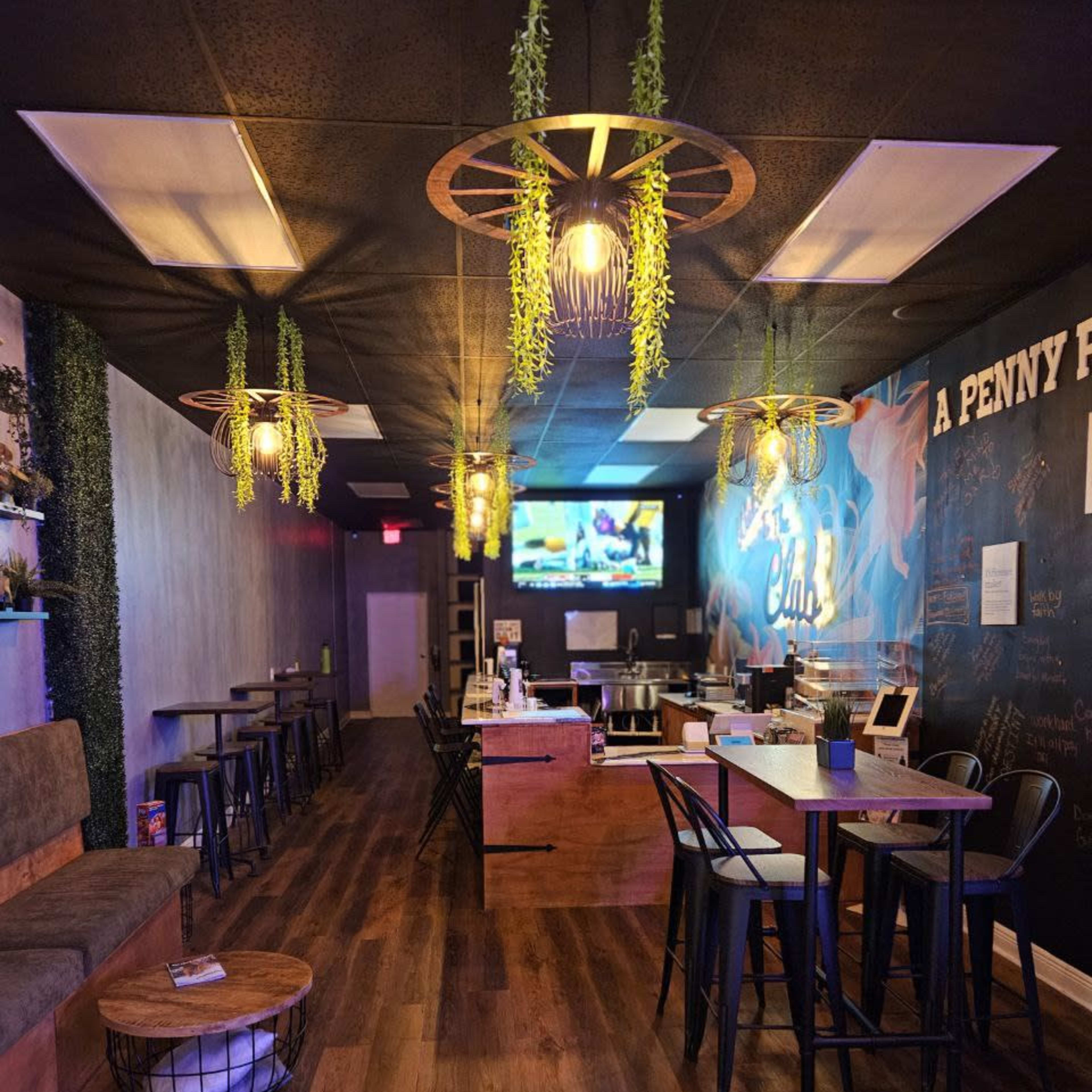 An indoor cafe with wooden flooring, modern furniture, and plants hanging from light fixtures.