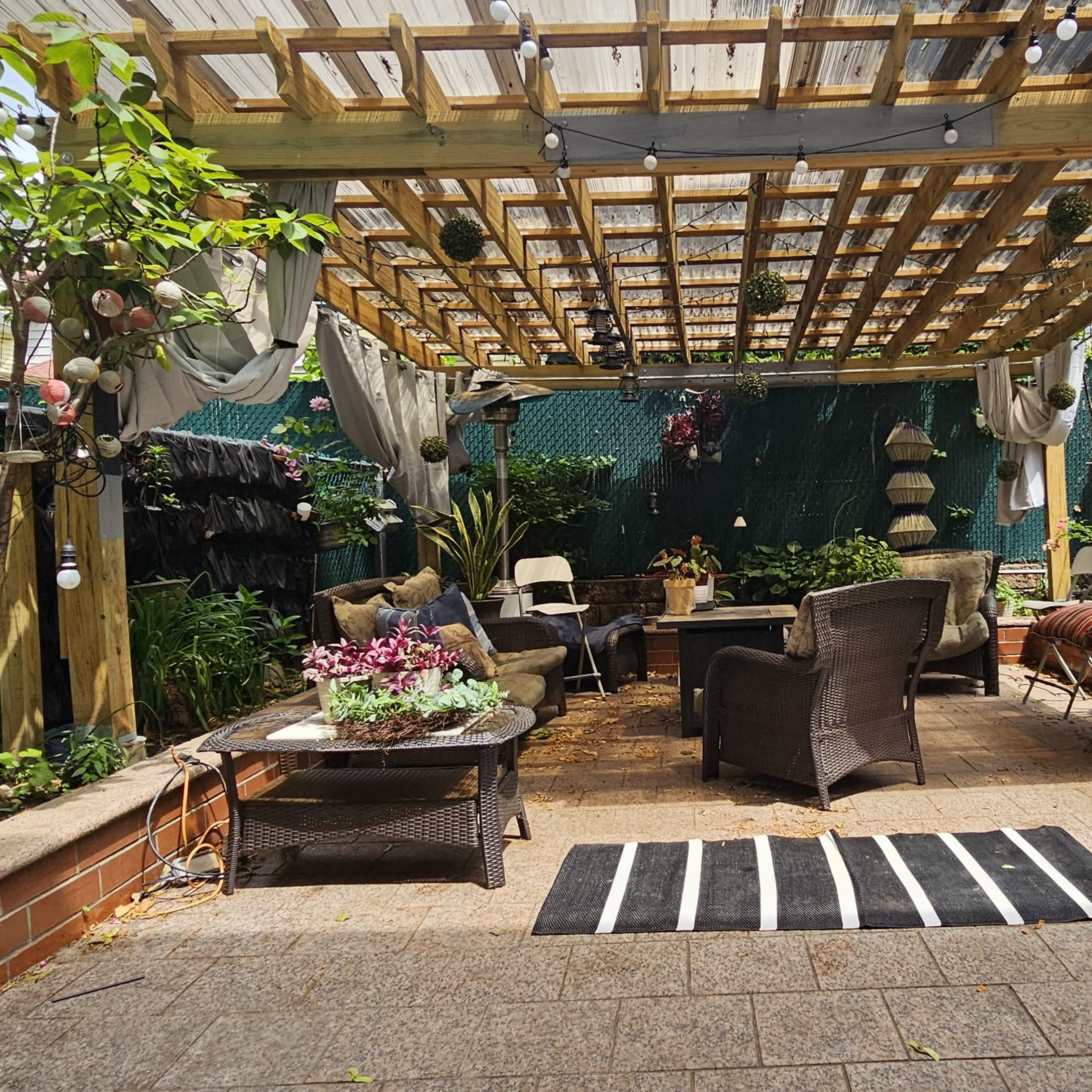 A landscaped patio area with a wooden trellis overhead, surrounded by potted plants and seating arrangements.