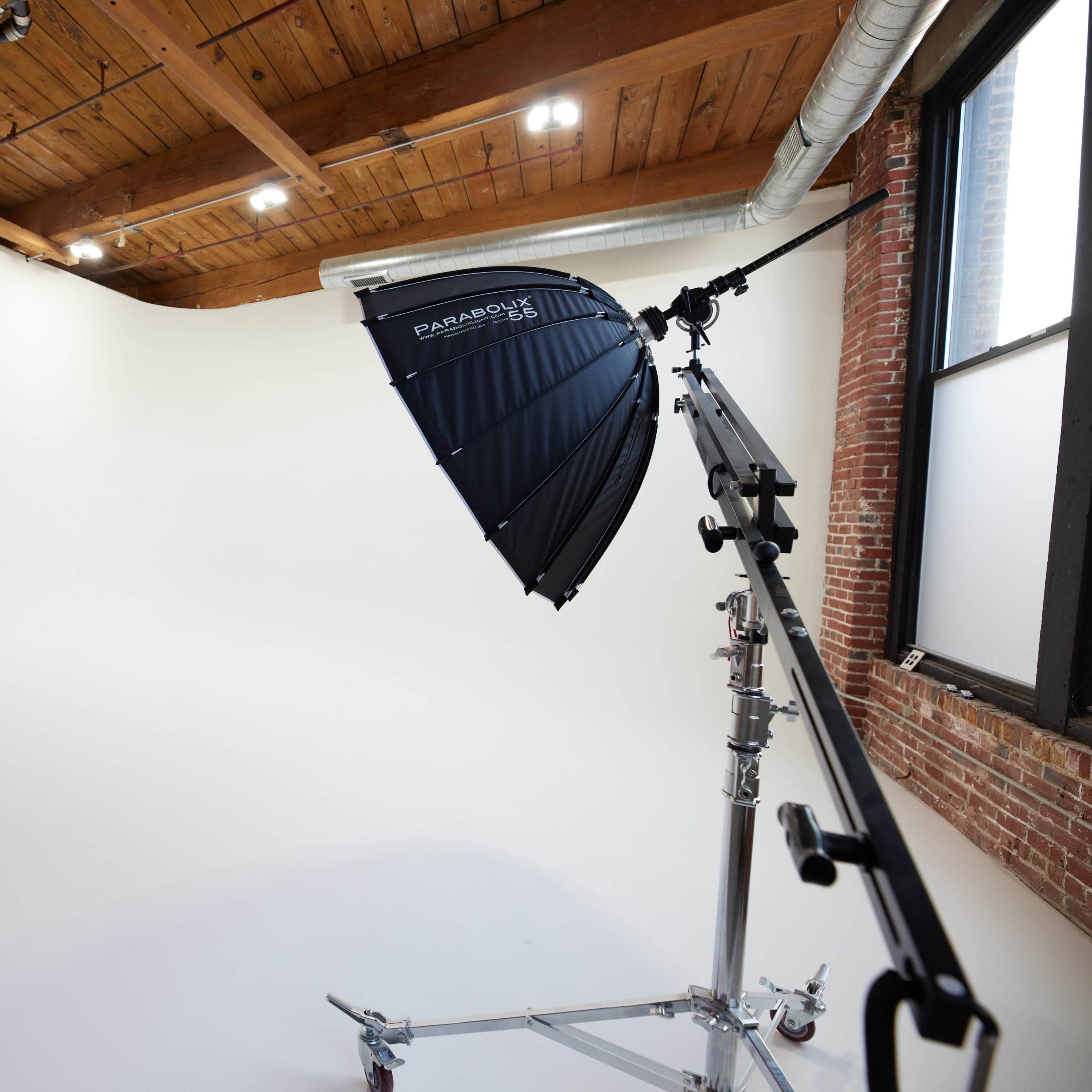 A photography studio with a white backdrop and a large umbrella light on a stand.