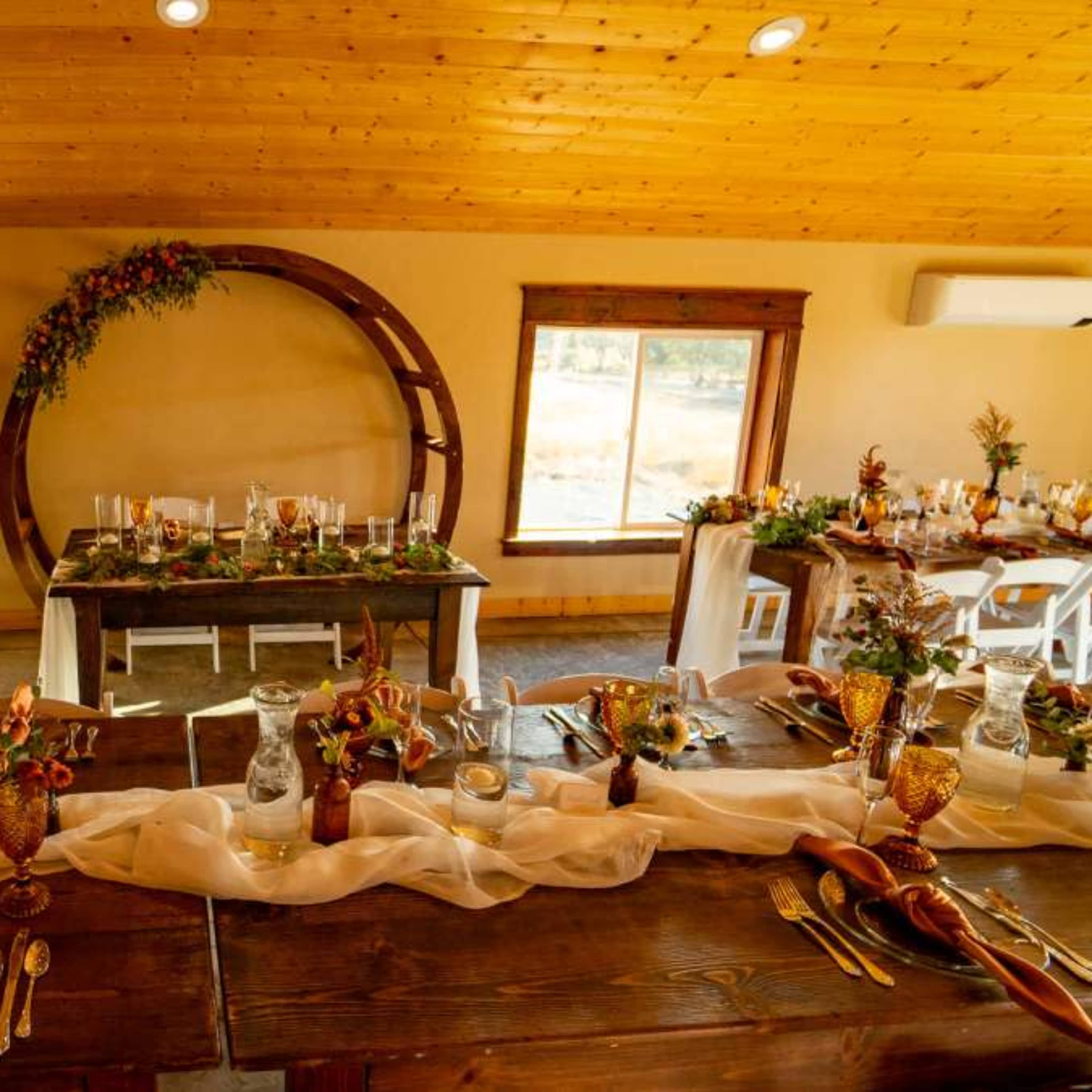 A banquet setting features elegantly arranged tables with floral centerpieces and a circular backdrop in a warmly lit room.