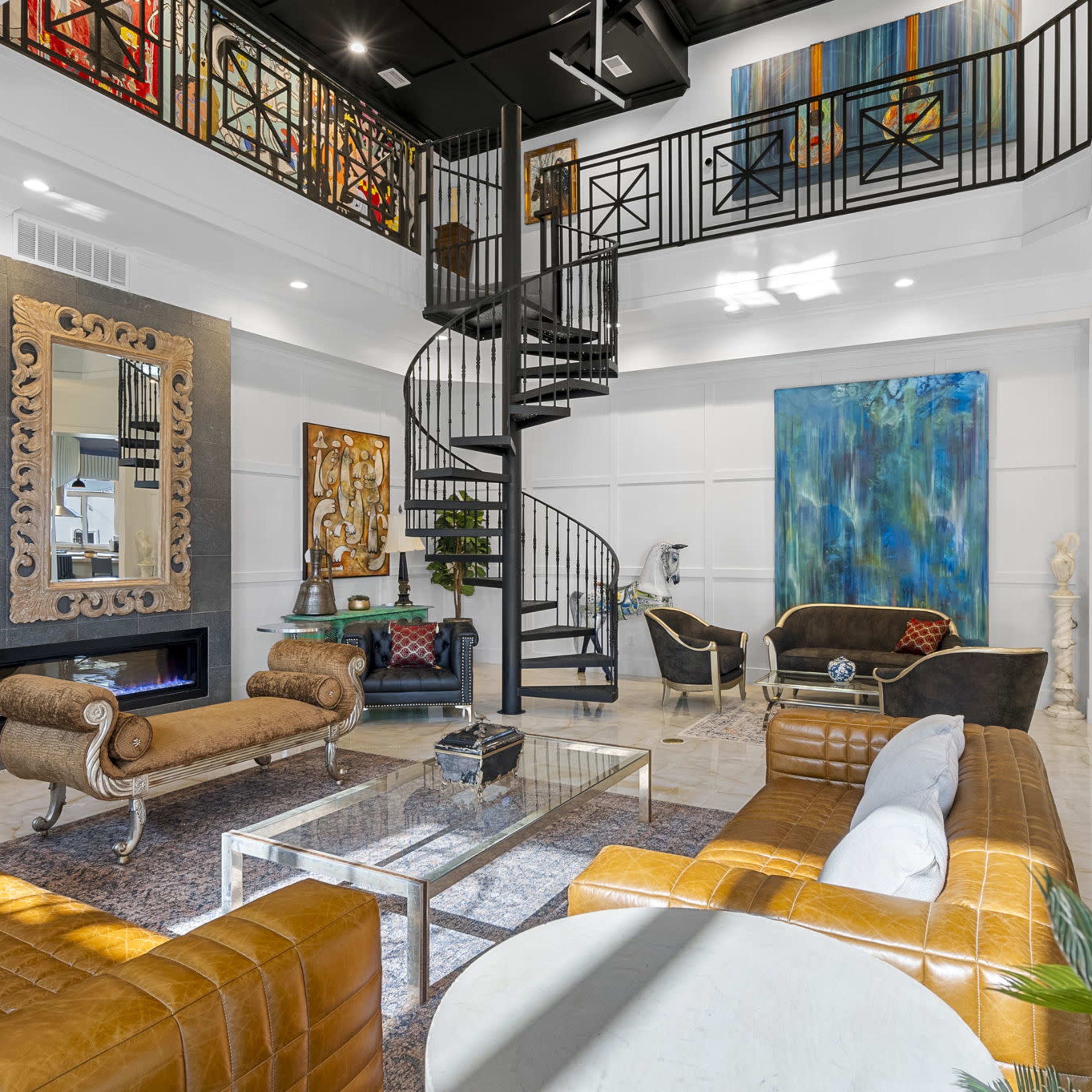 A spacious and modern living room featuring a spiral staircase, a large mirror, and various artworks on the walls, with elegant furnishings arranged around a coffee table.