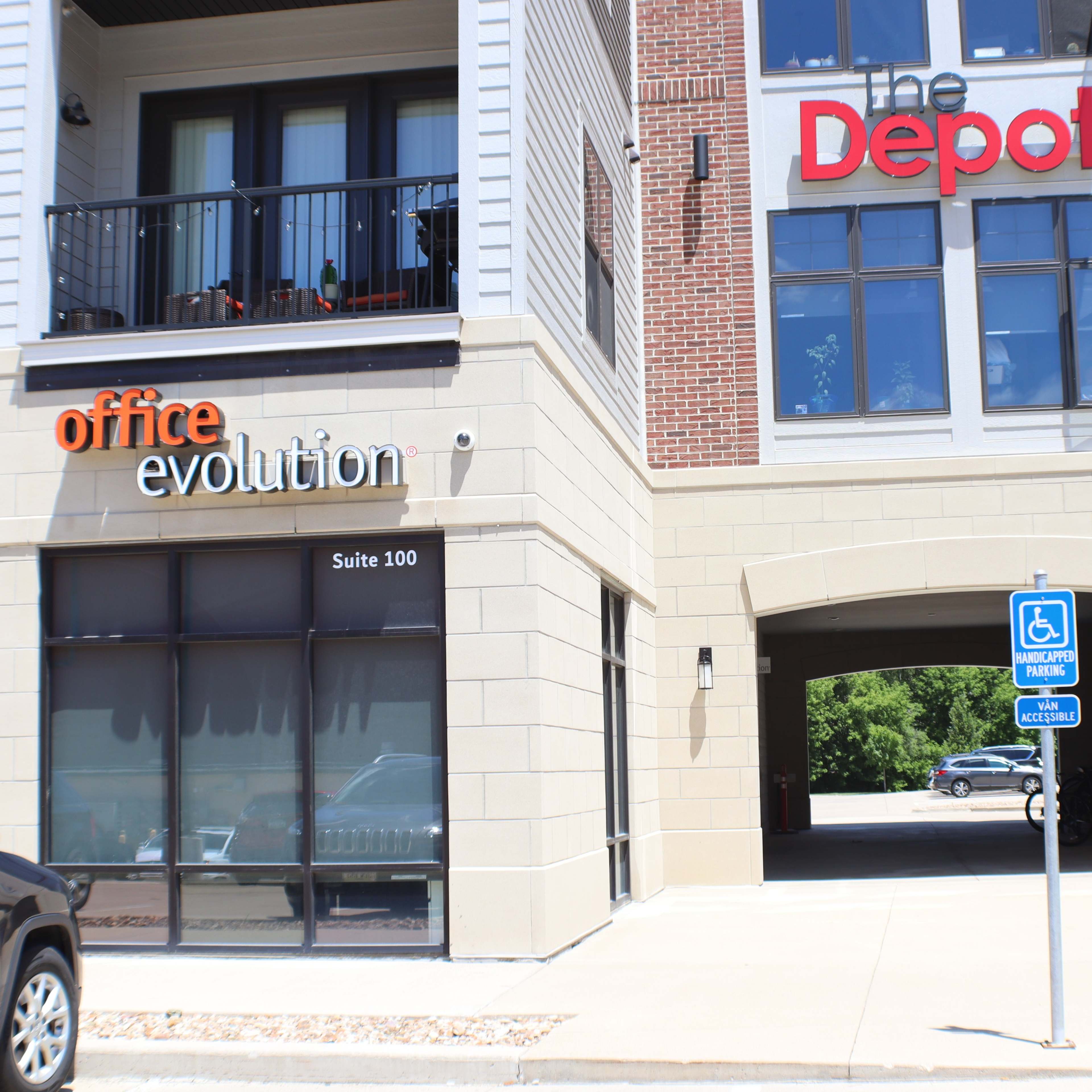 A commercial building featuring a sign for "office evolution" and another for "the Depot," along with a designated parking space for the handicapped.