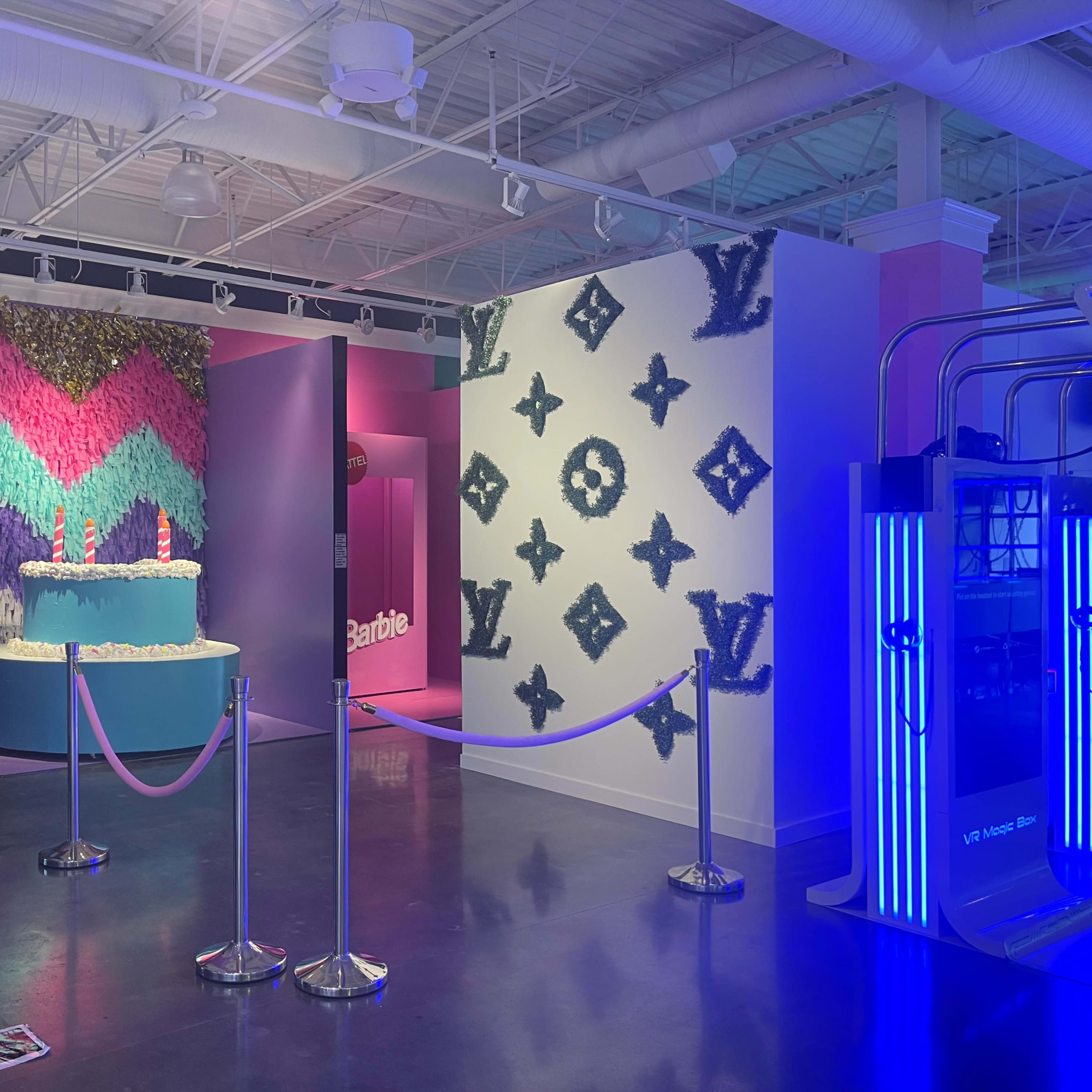 An interior space featuring vibrant walls with a pink and green zigzag design, a blue display with the "Barbie" logo, and a white wall adorned with a Louis Vuitton pattern.