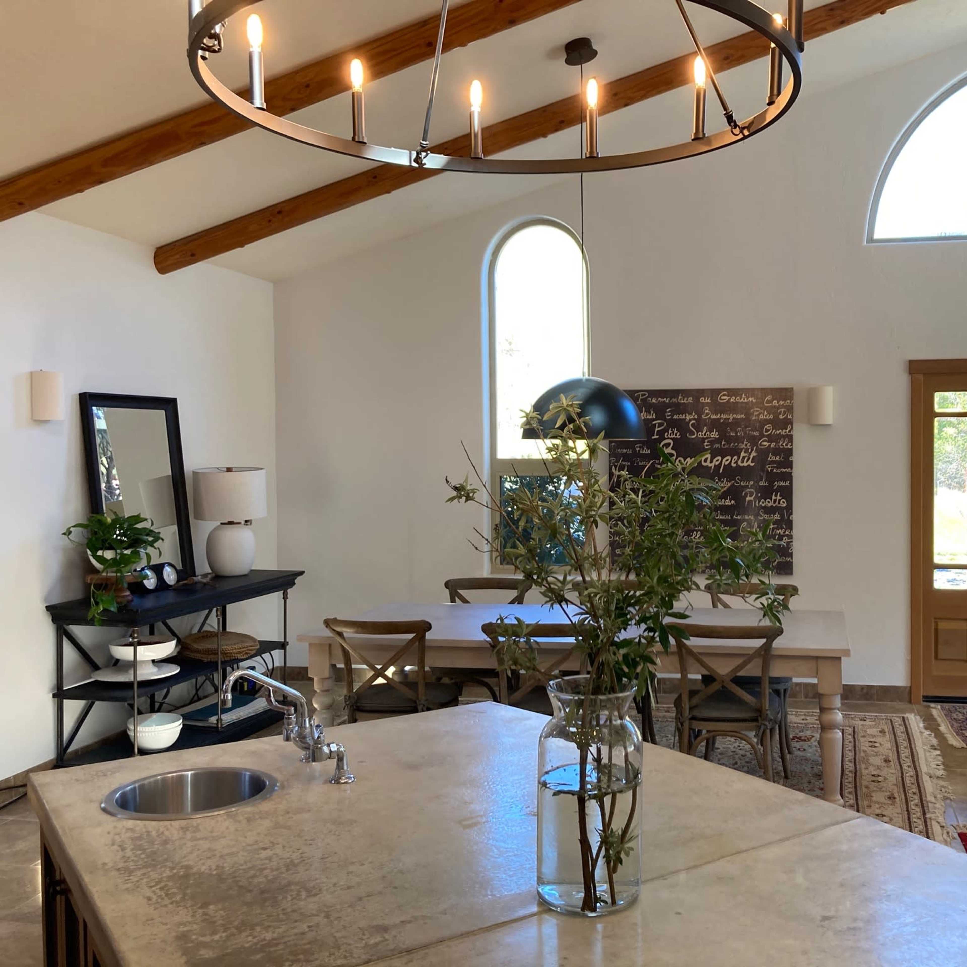 A spacious kitchen and dining area featuring a large island with a sink, a wooden dining table, and a front door with large windows.