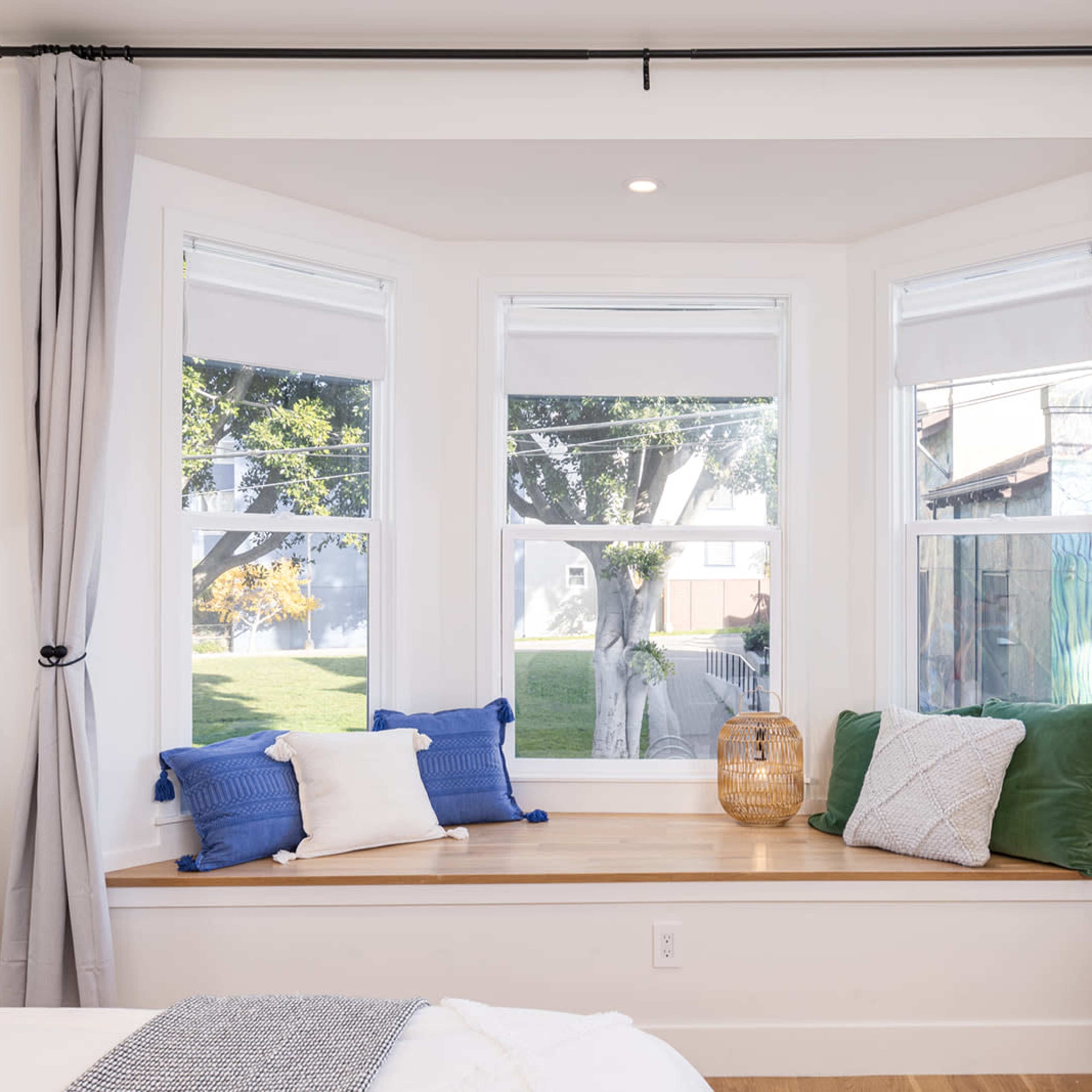 A bright bedroom features a bay window with a wooden ledge, adorned with cushions and natural light streaming in.