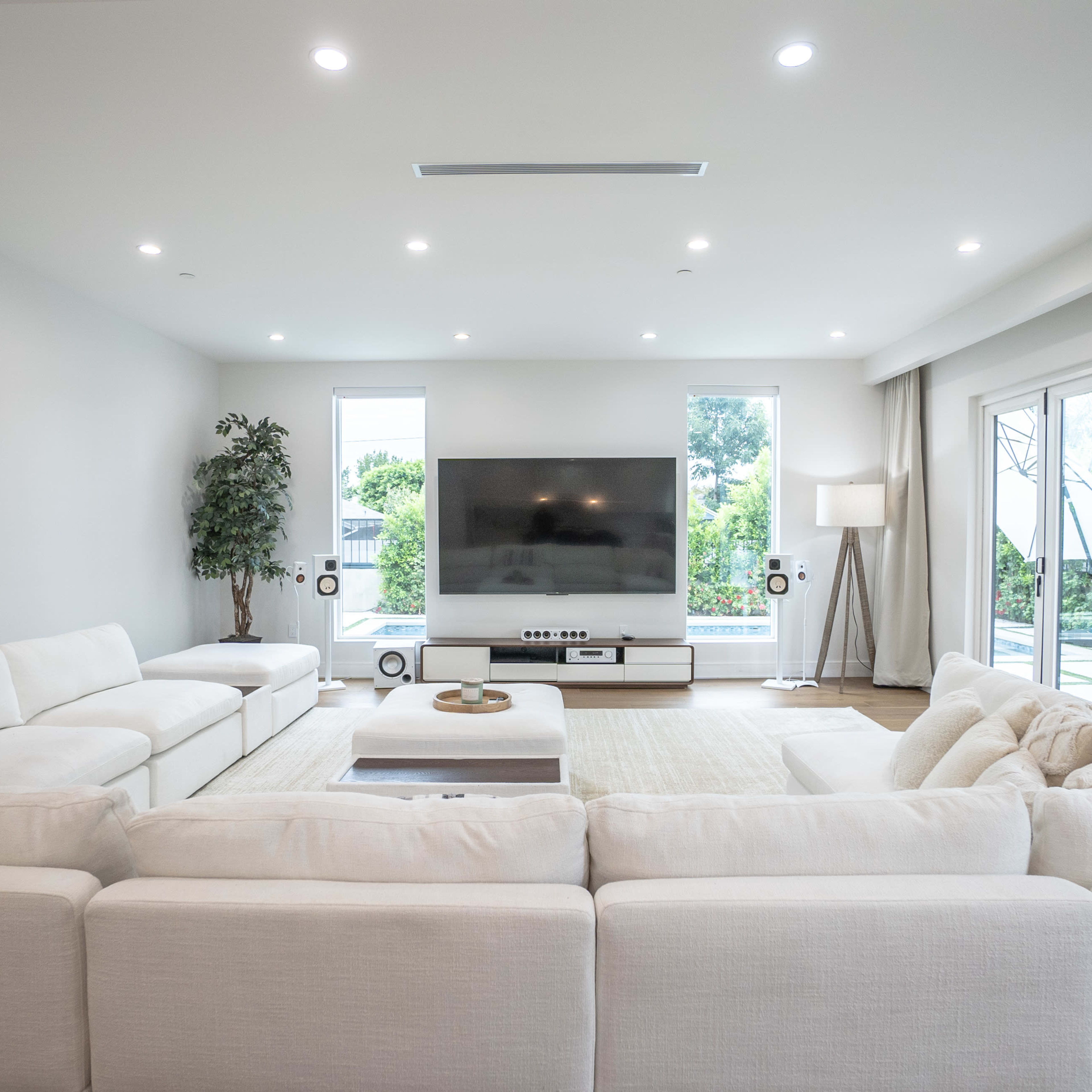 A modern living room features a large sectional sofa, a flat-screen television, and glass doors leading to an outdoor space.