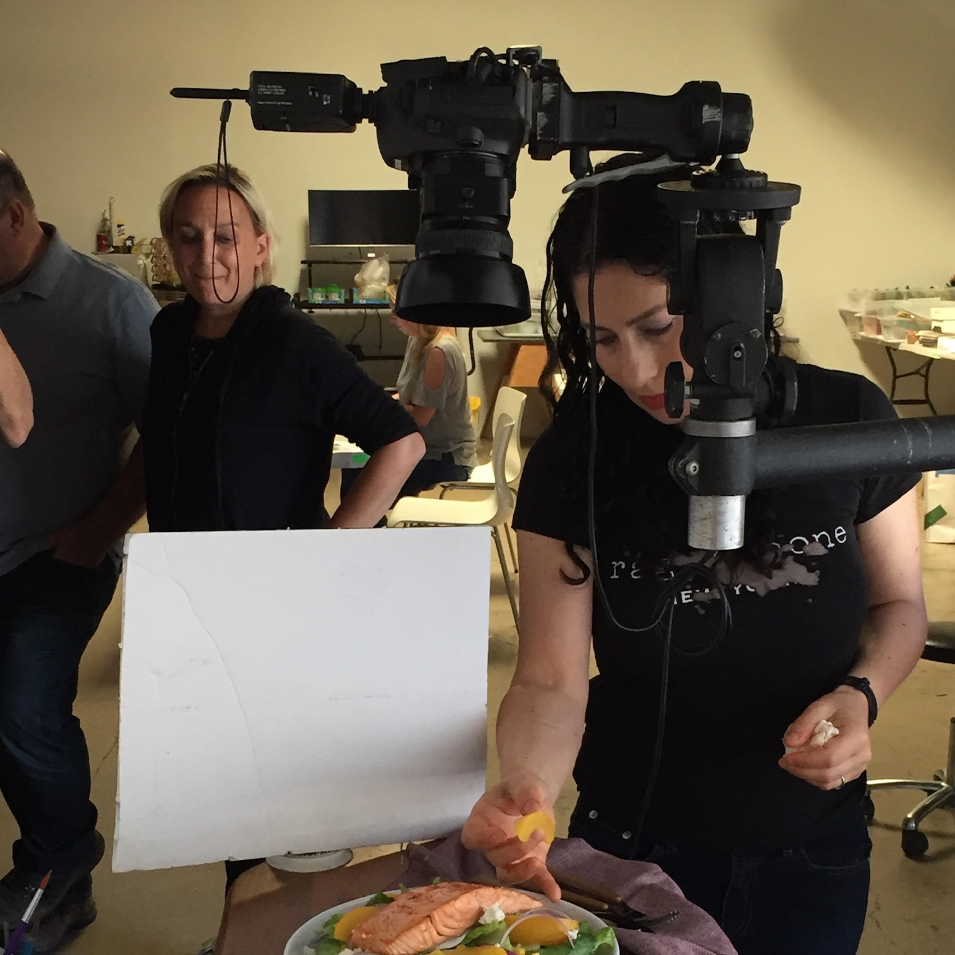 A woman garnishes a plate of salad with salmon under a camera set up in a photography studio.
