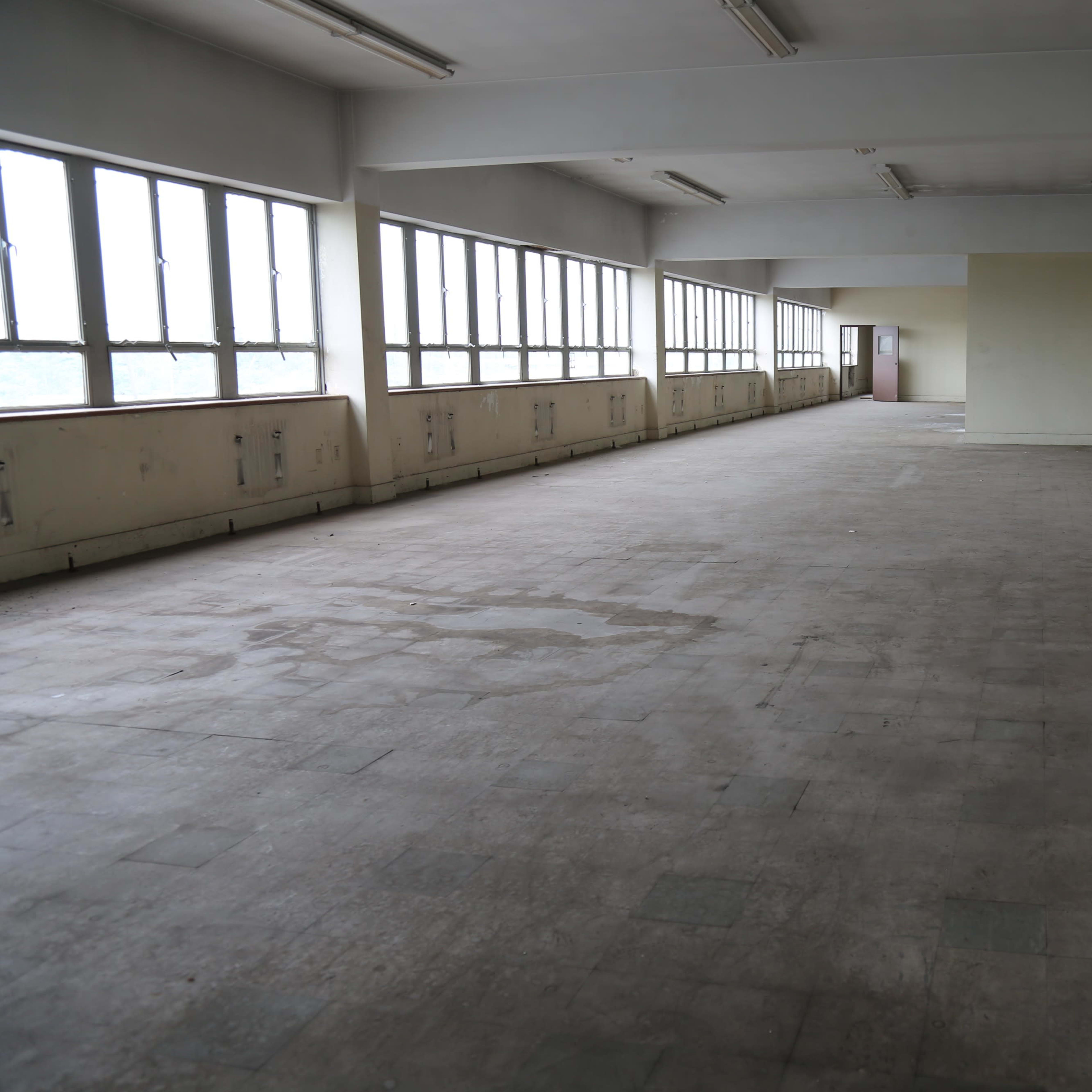 An empty, unadorned room with large windows and a tiled floor.